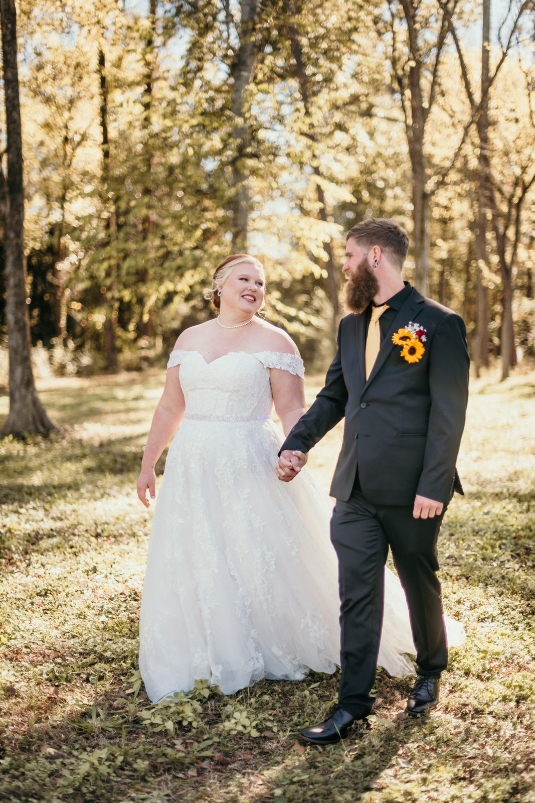 A couple in wedding attire share a joyful moment while holding hands in a sunlit autumn forest setting.