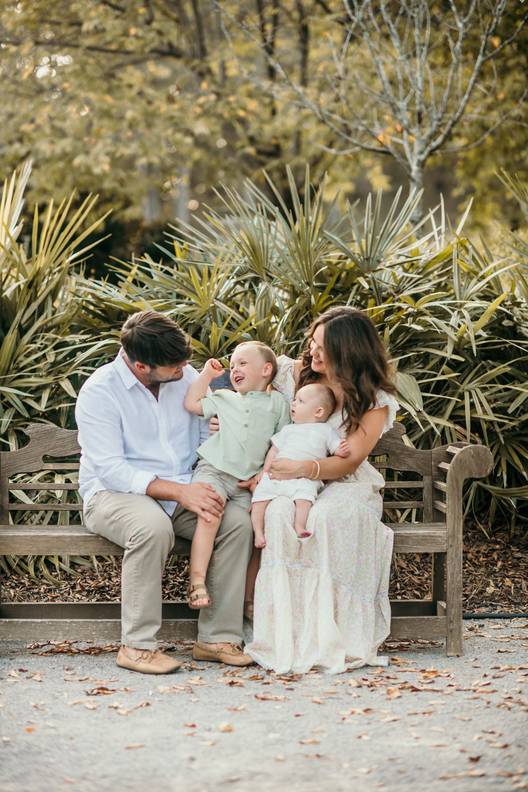 Family shares intimate moment while sitting on wooden bench in garden setting.