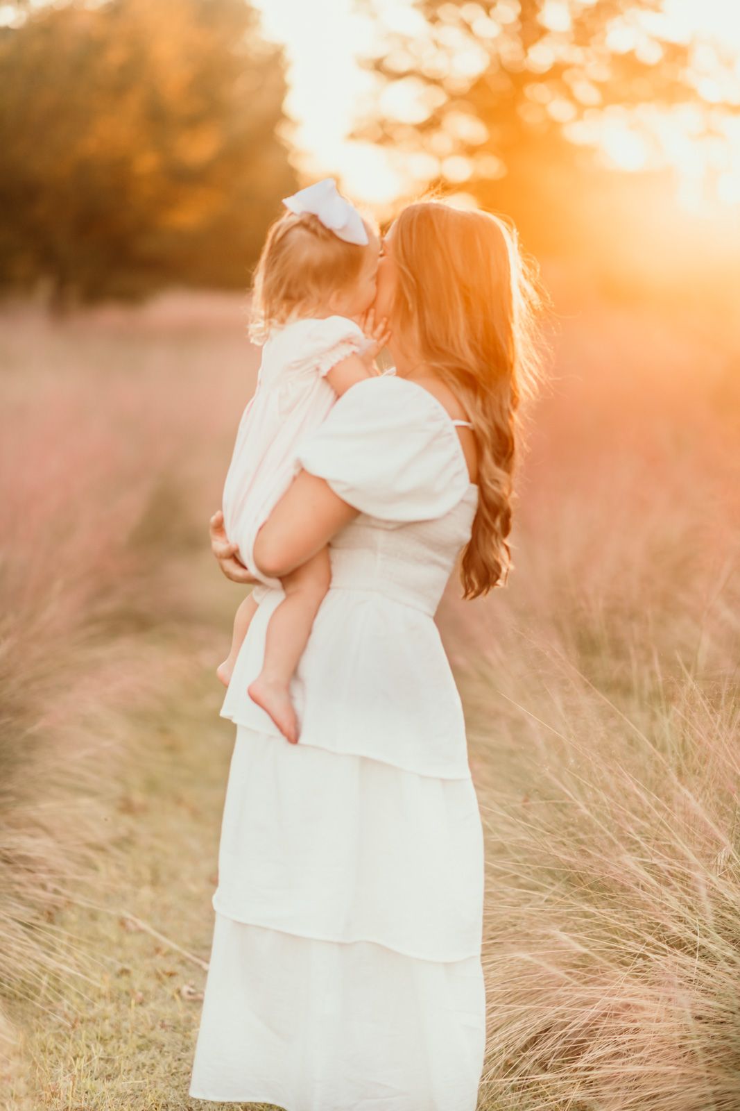 A tender moment captured in a golden sunset field with flowing grass and soft white clothing.