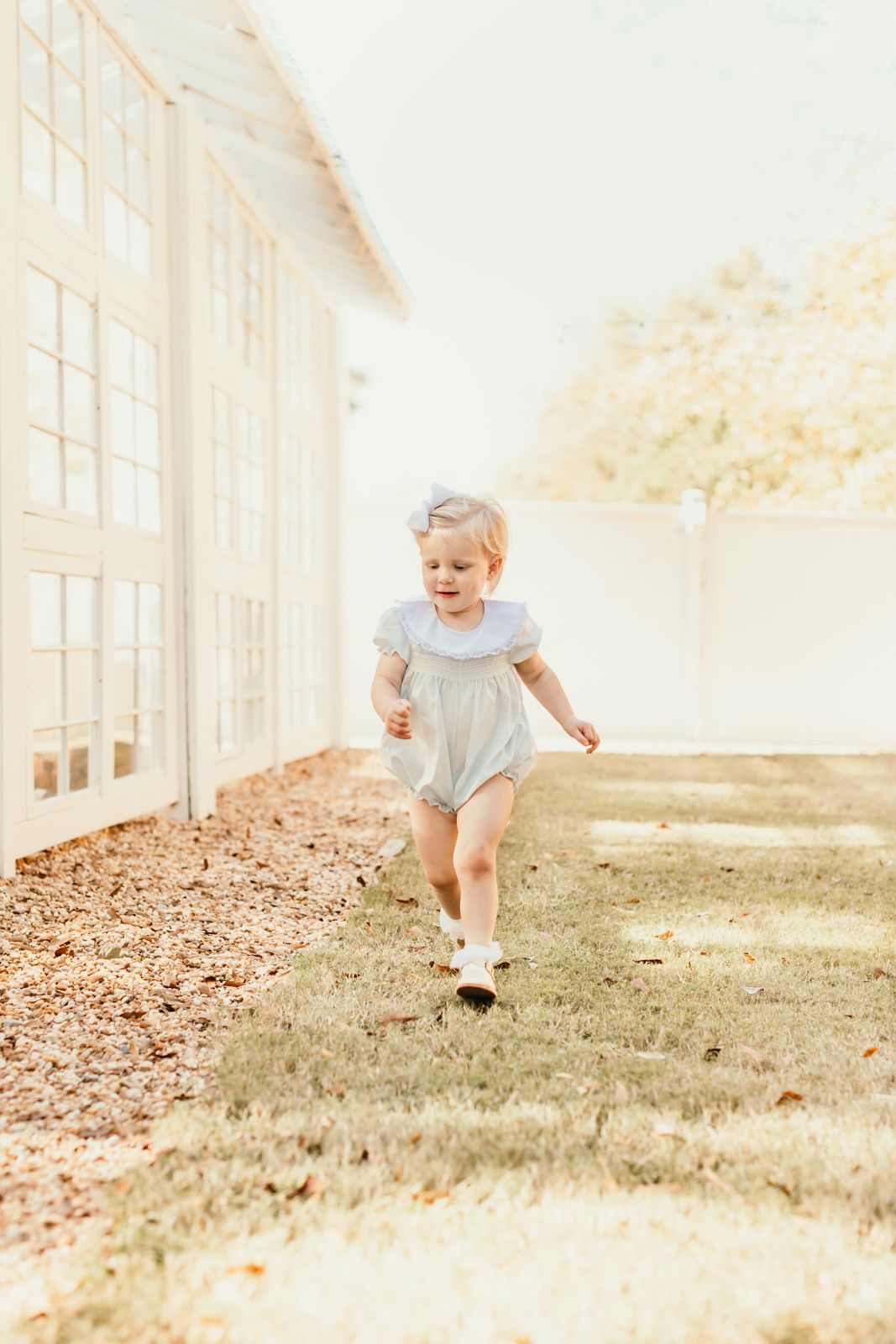 A child runs joyfully across a sunlit lawn beside a white building.