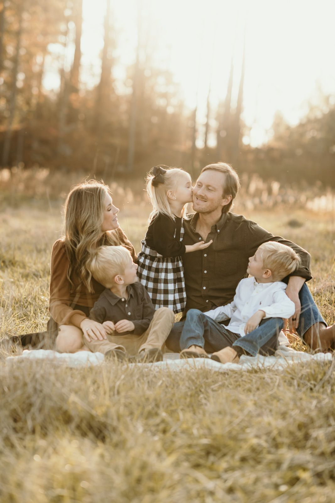 A family shares joyful moments together while laying in golden sunlit grass during an outdoor photo session.
