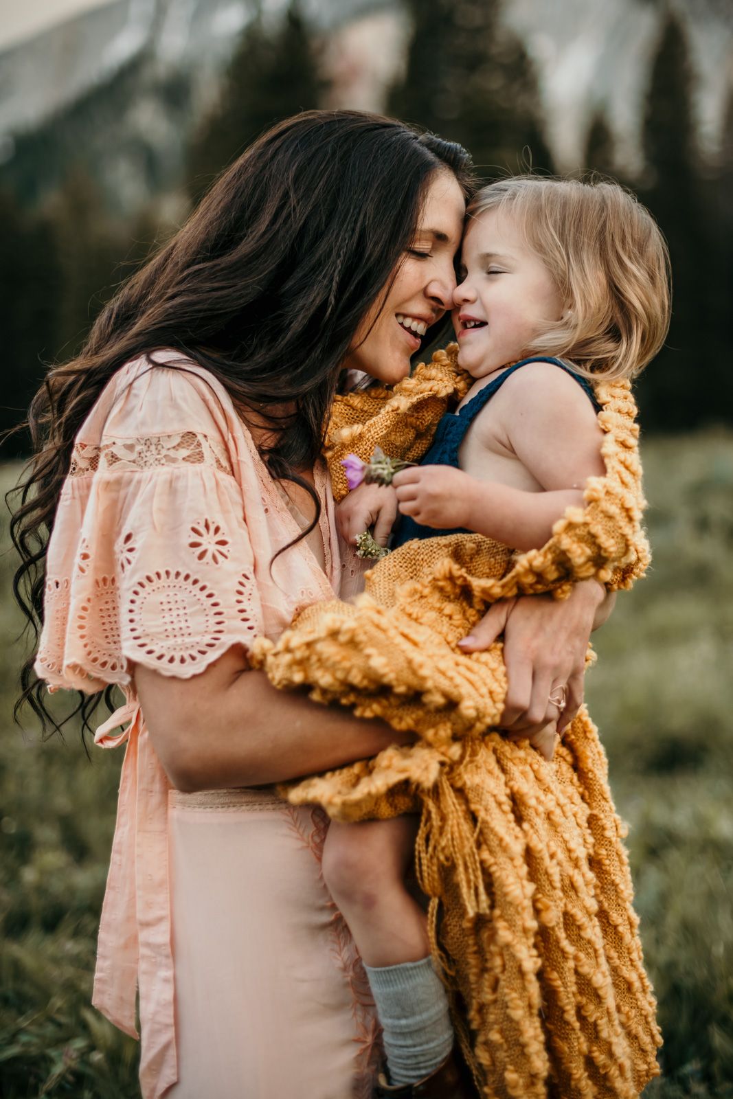Two people in pink and mustard yellow outfits embrace lovingly in an outdoor setting during golden hour.