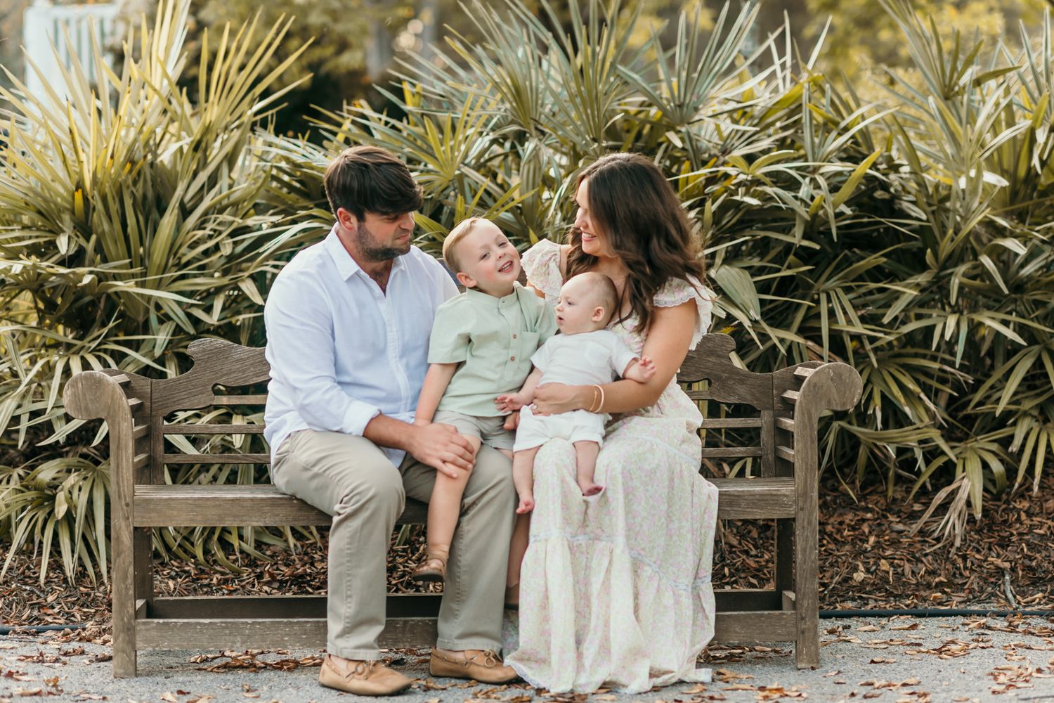 Family sitting together on wooden bench surrounded by tropical plants.