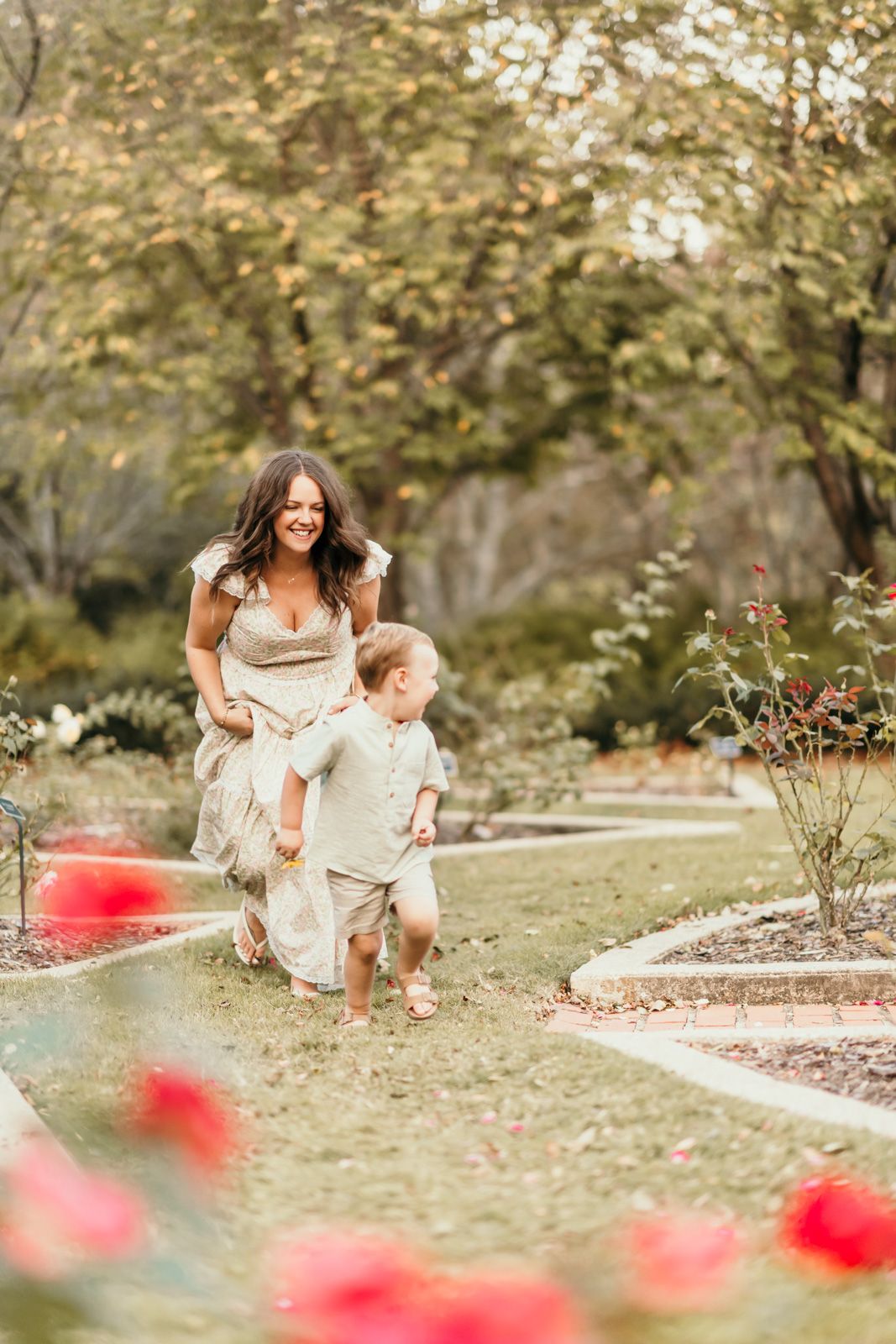 A joyful outdoor photoshoot in a garden with blooming red flowers and soft natural lighting.