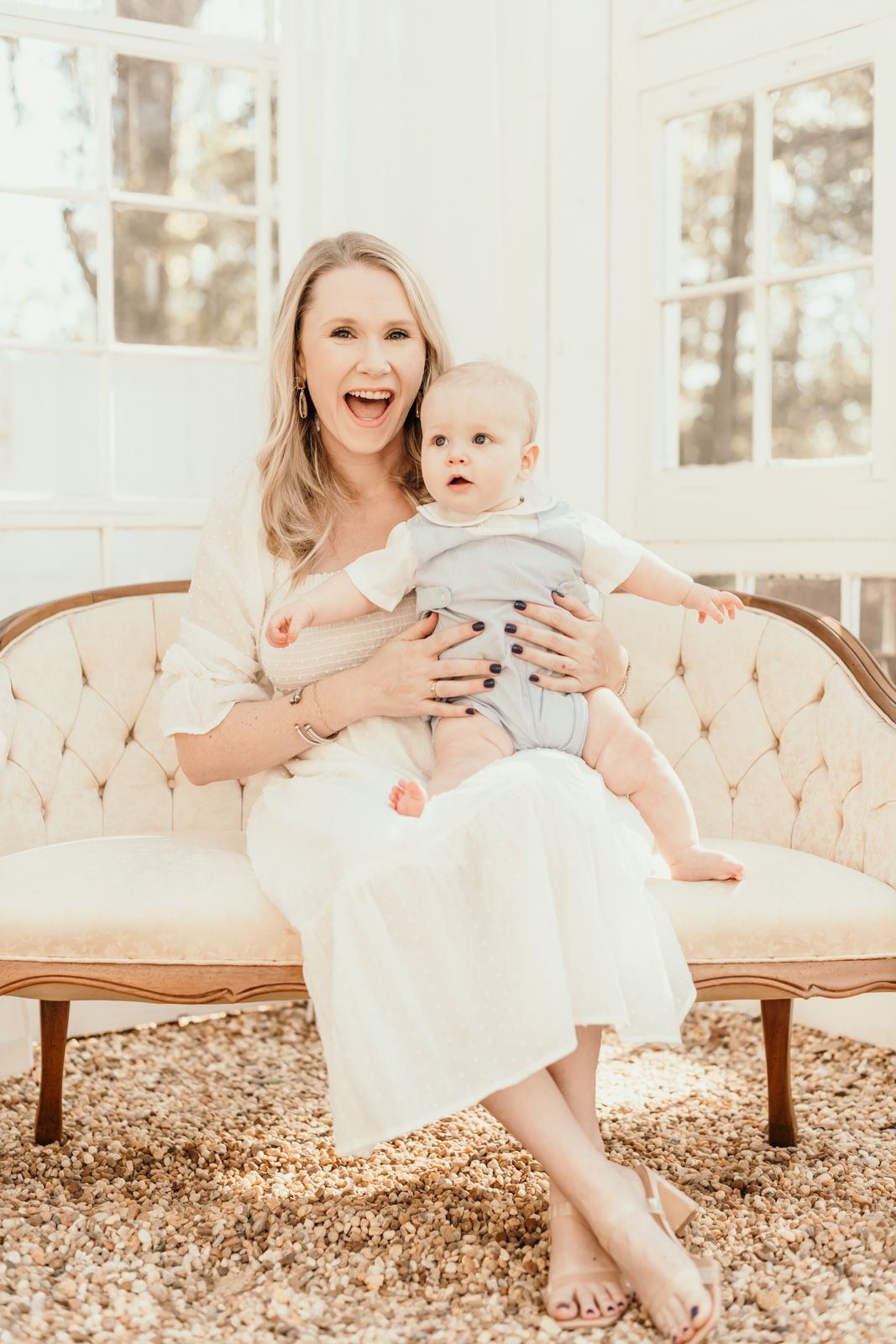 Family portrait session on an elegant cream-colored settee in a sunlit room.