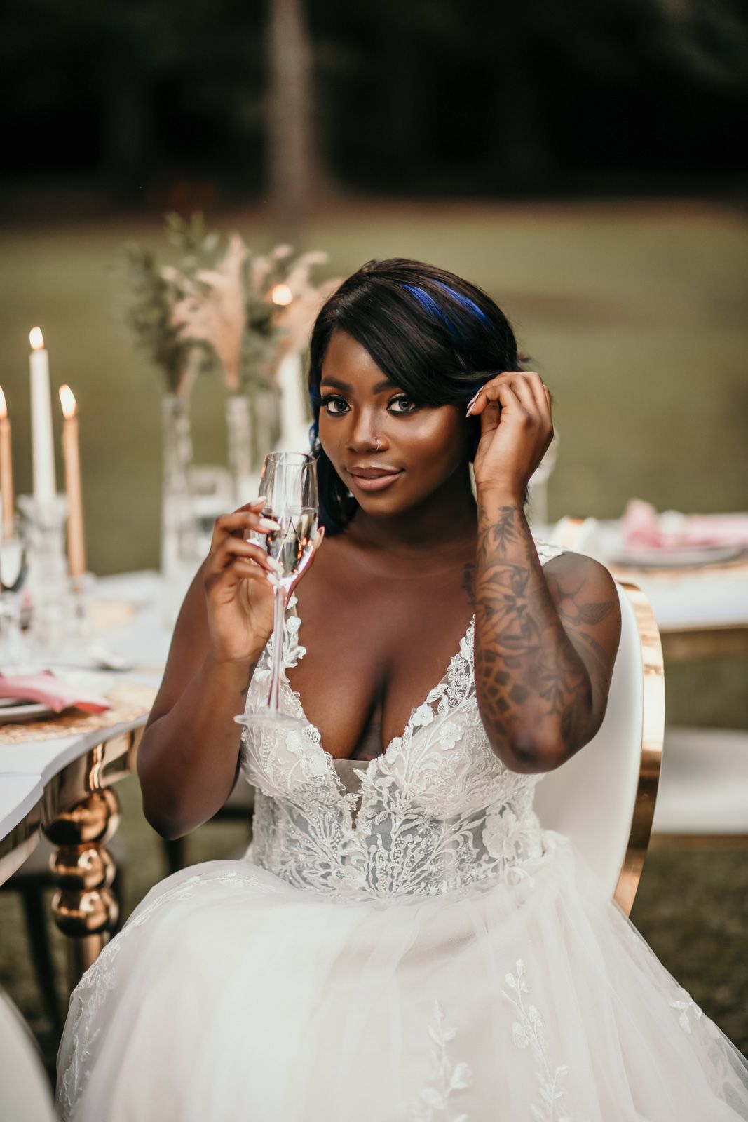 Beautiful bride in a white lace wedding dress poses elegantly with lit candles at an outdoor reception.