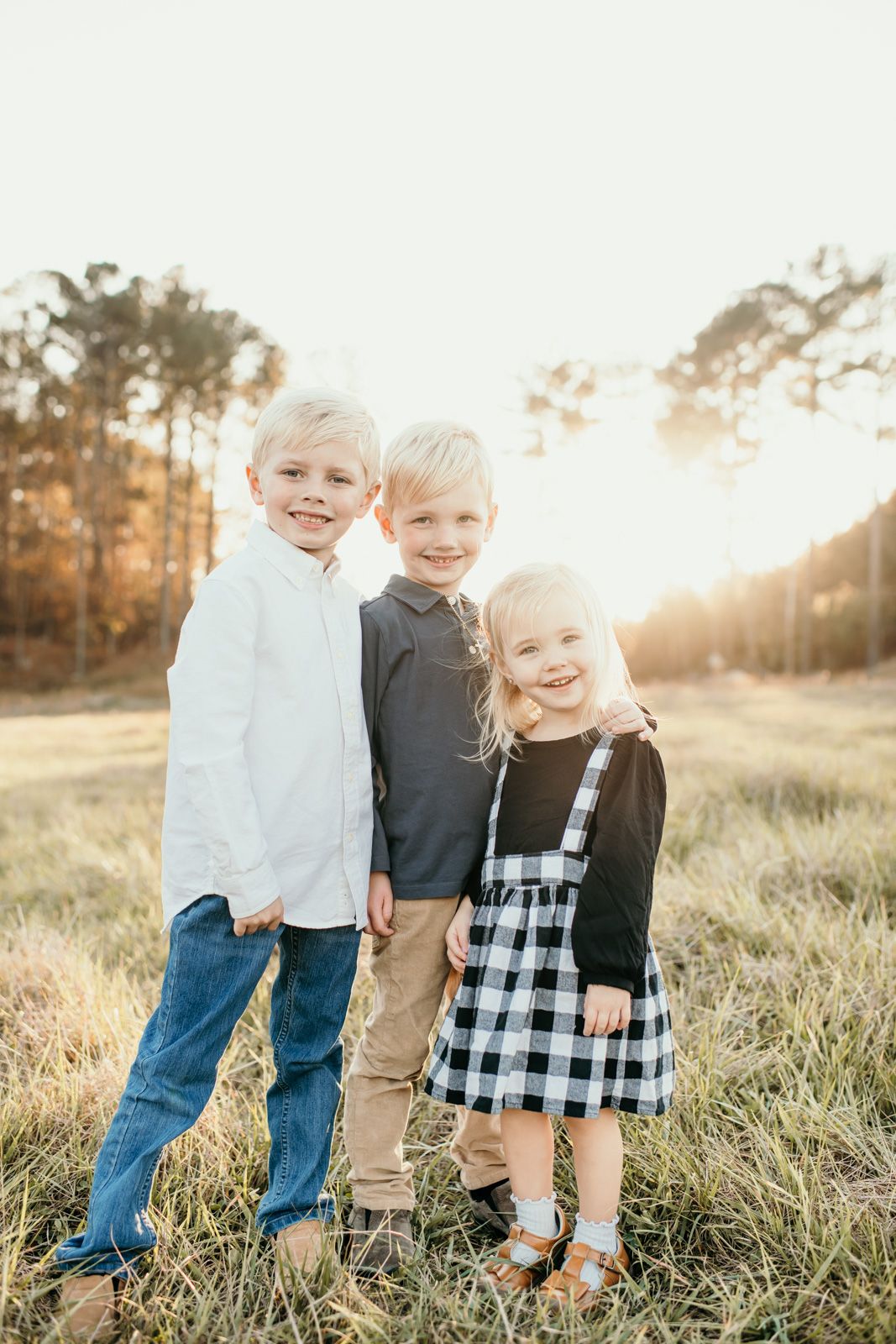 Three children play together in a sun-lit field with tall grass at golden hour.