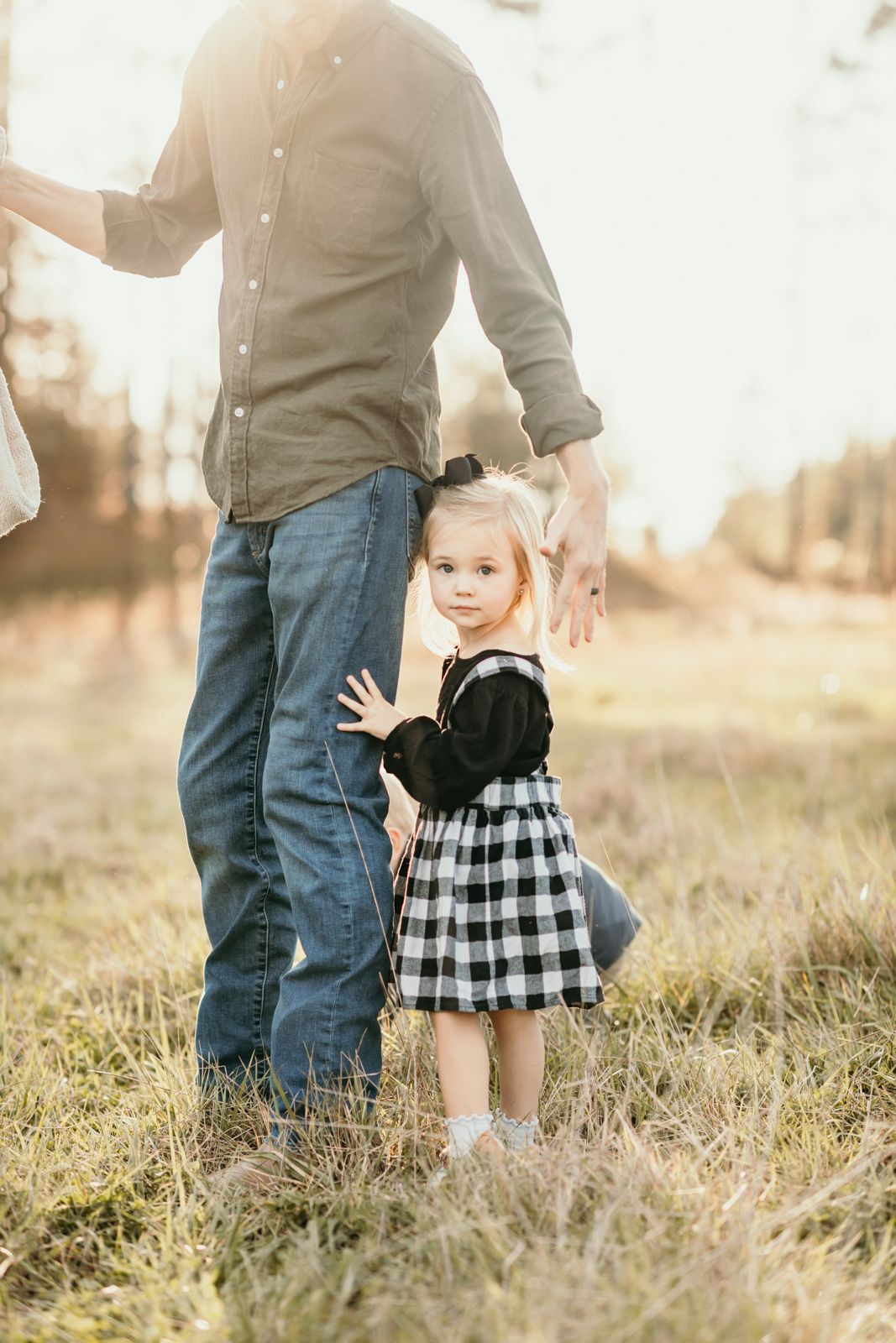 Parent and toddler in black and white checkered dress walking together through sunlit grassy field at sunset.