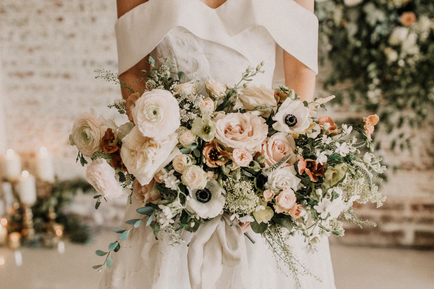 Delicate white and blush floral wedding arrangements with roses and greenery against a brick wall.