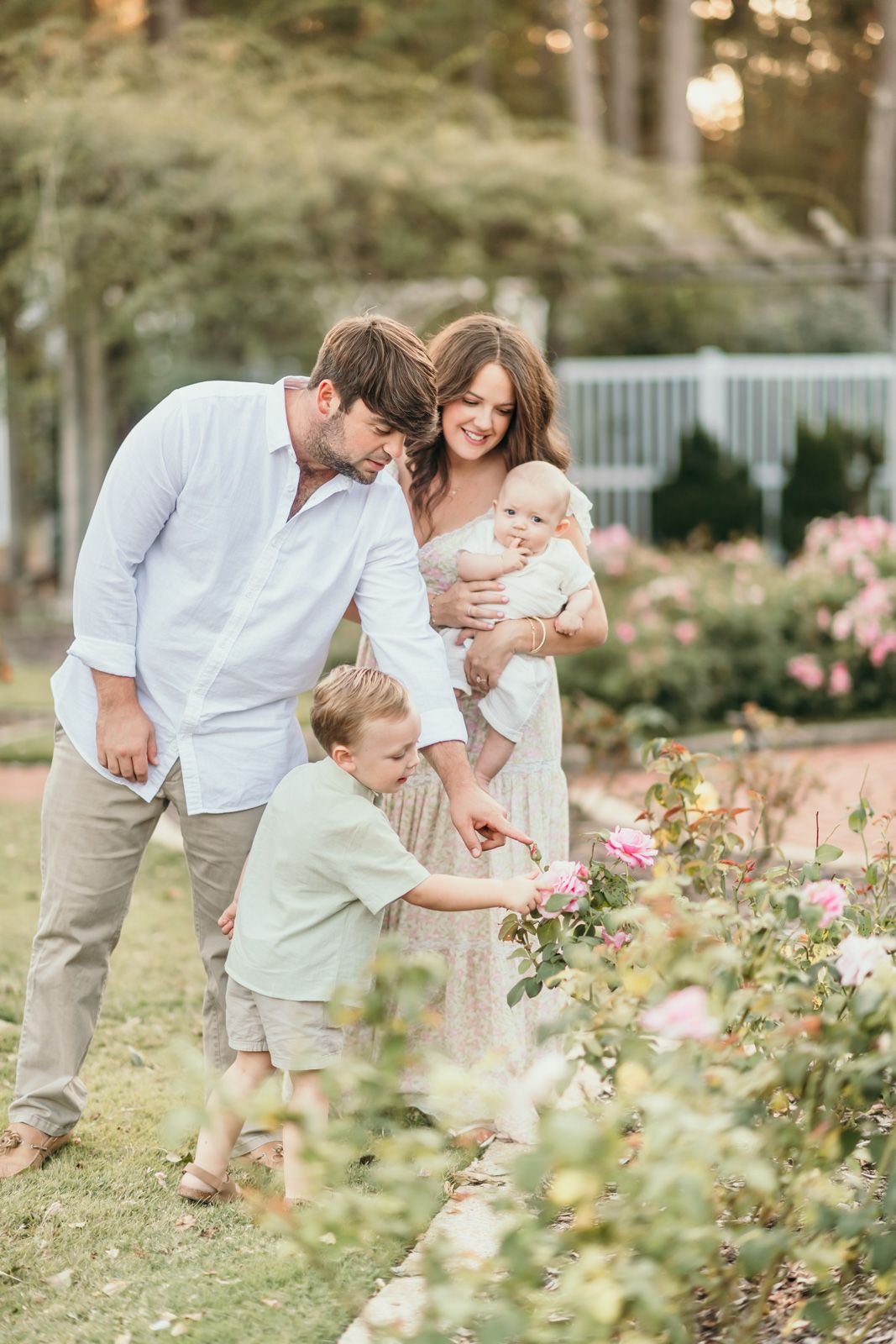 A family shares tender moments together in a sunlit garden with blooming pink roses.