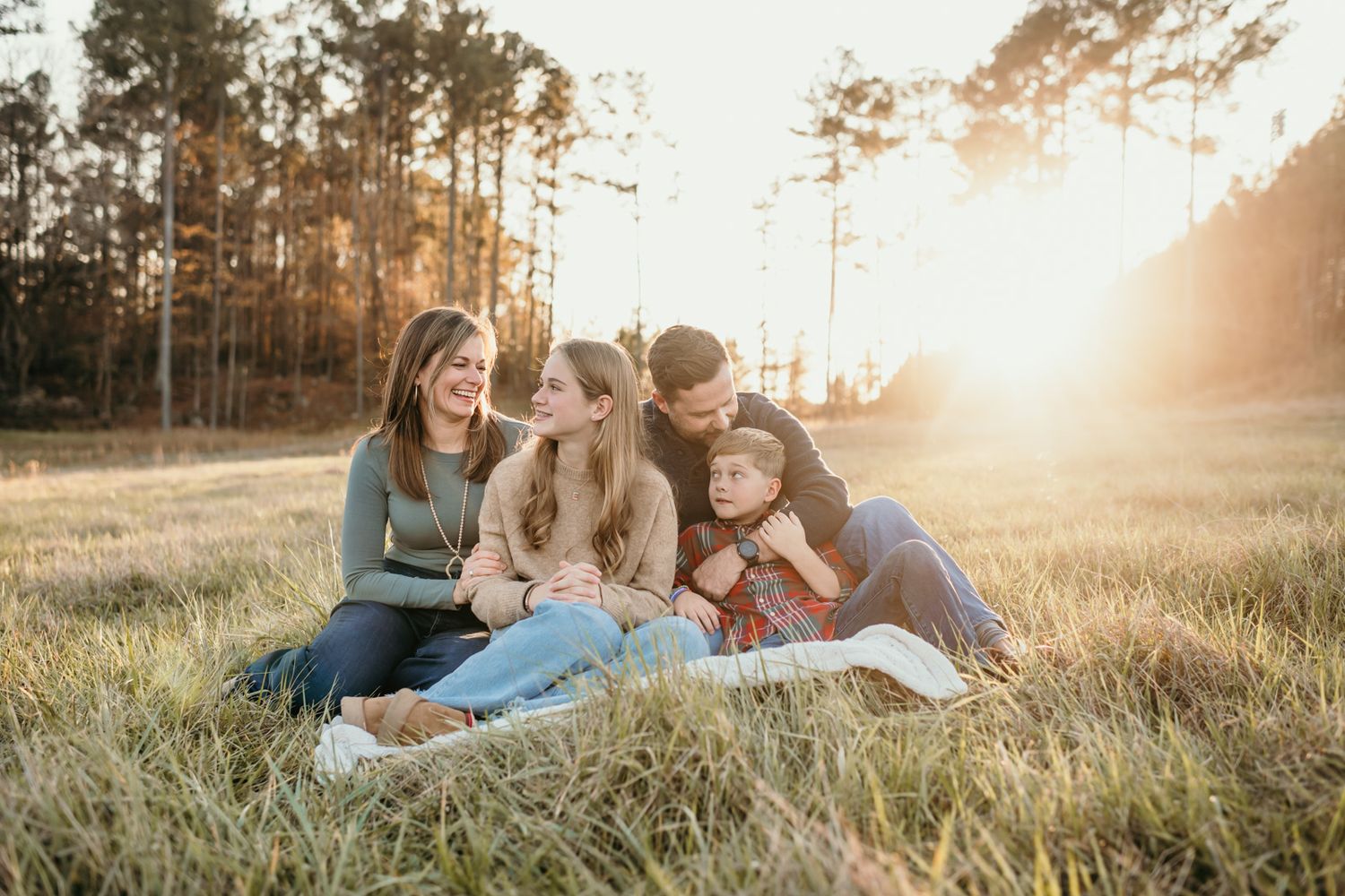 Family relaxing together in a grassy field during golden hour sunset.