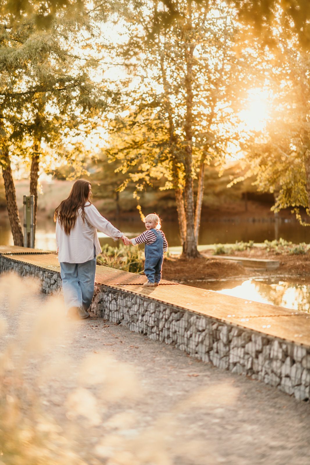A family walks along a stone wall path during golden hour sunset as sunlight filters through autumn trees.