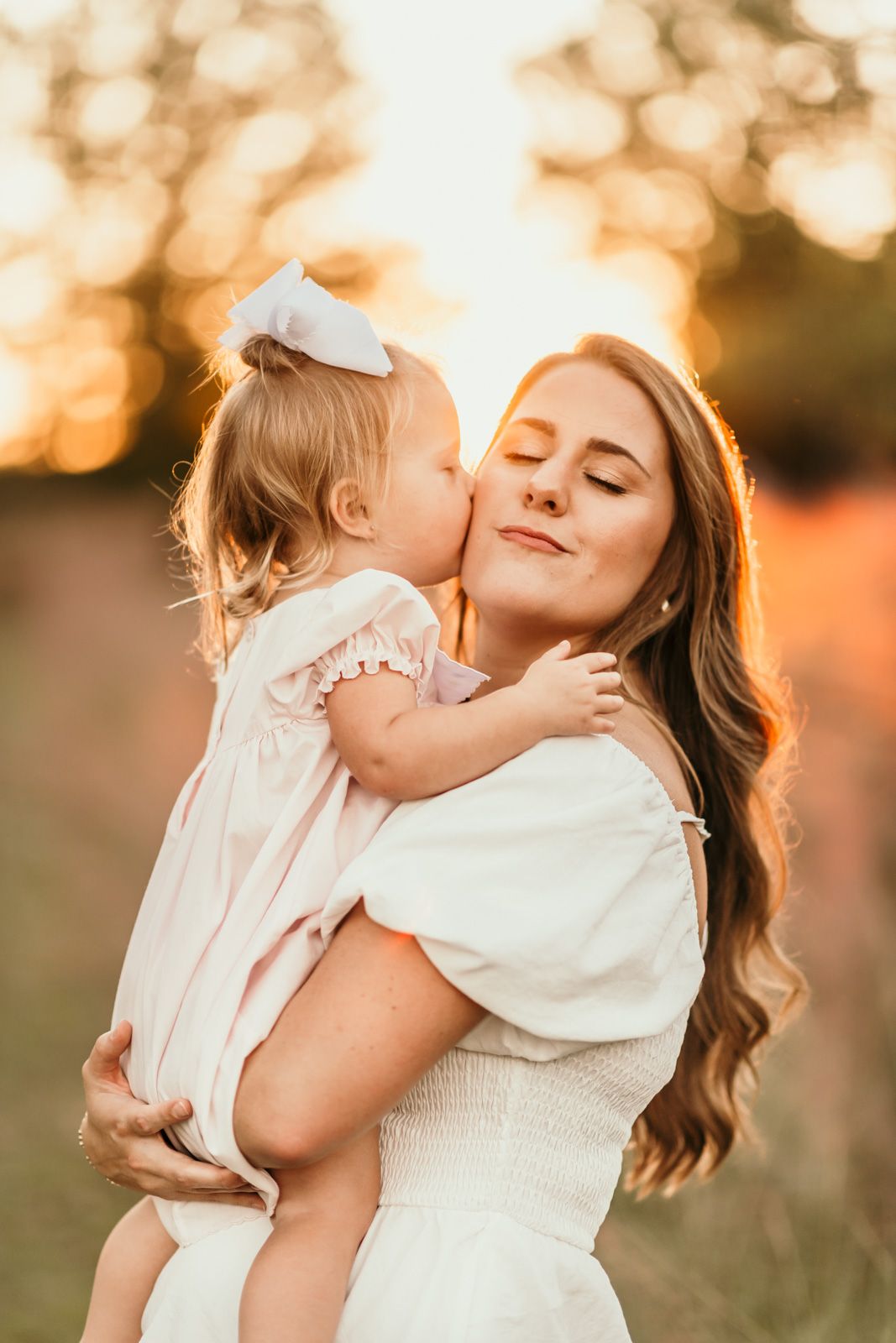 A tender embrace between parent and child silhouetted against a warm sunset with bokeh lighting effects in the background.