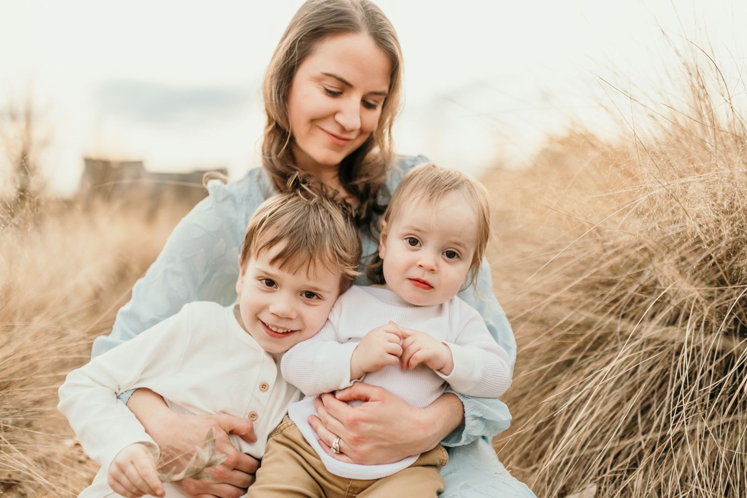 A family sits together in a golden field during sunset creating intimate lifestyle portraits.