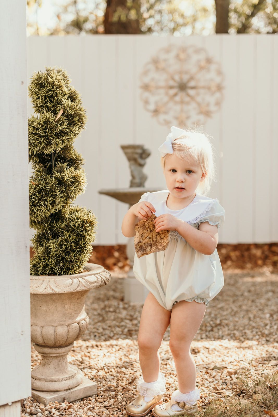 Toddler exploring garden setting with decorative potted plants and natural lighting.