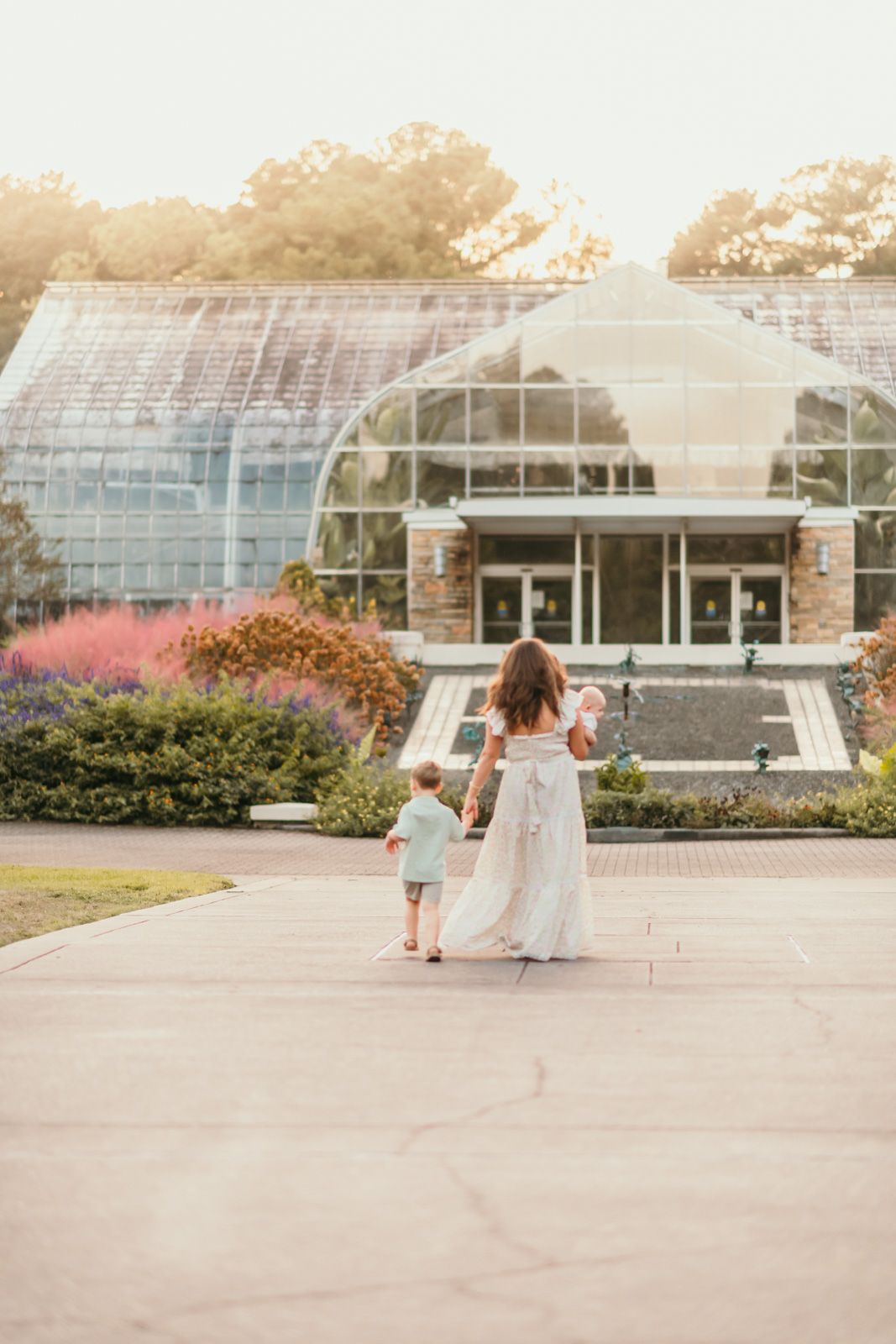 Family walking together outside a large greenhouse building during golden hour.