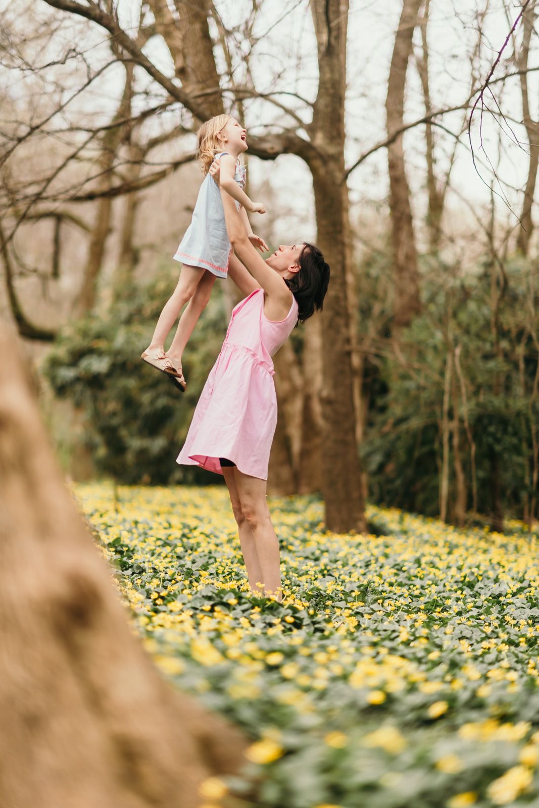 A person in a pink dress twirls joyfully in a spring forest filled with blooming yellow daffodils.