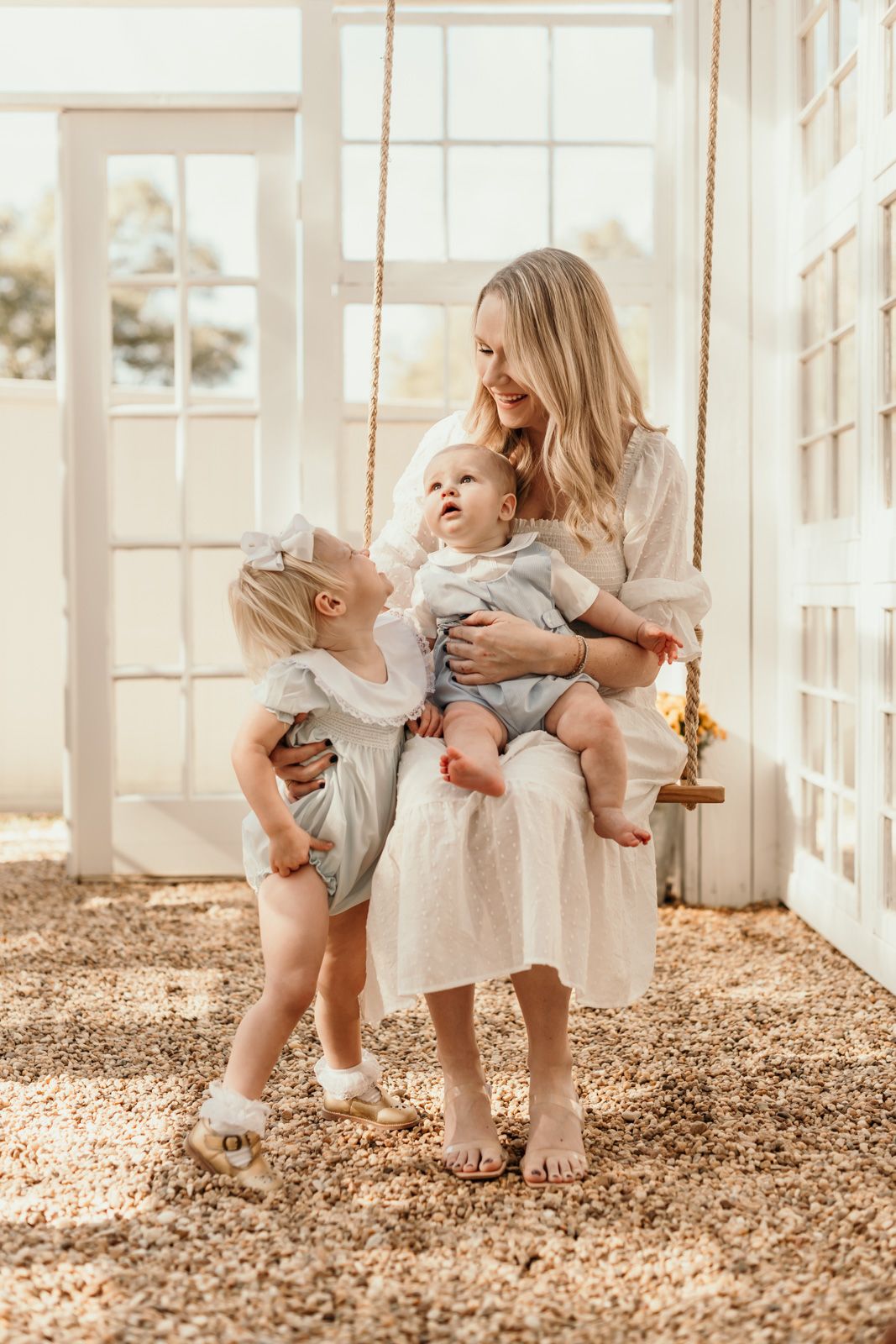 Joyful indoor photo session with a wooden swing and natural window lighting.