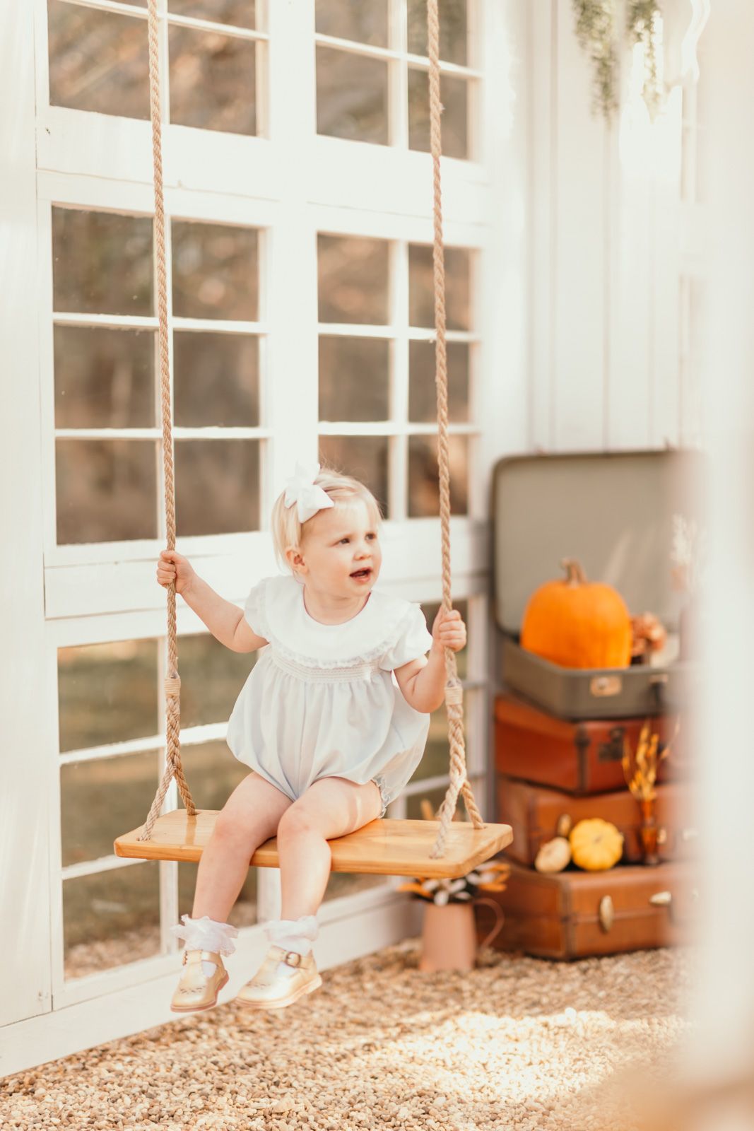 Wooden rope swing hangs in front of white French doors with orange pumpkins nearby.