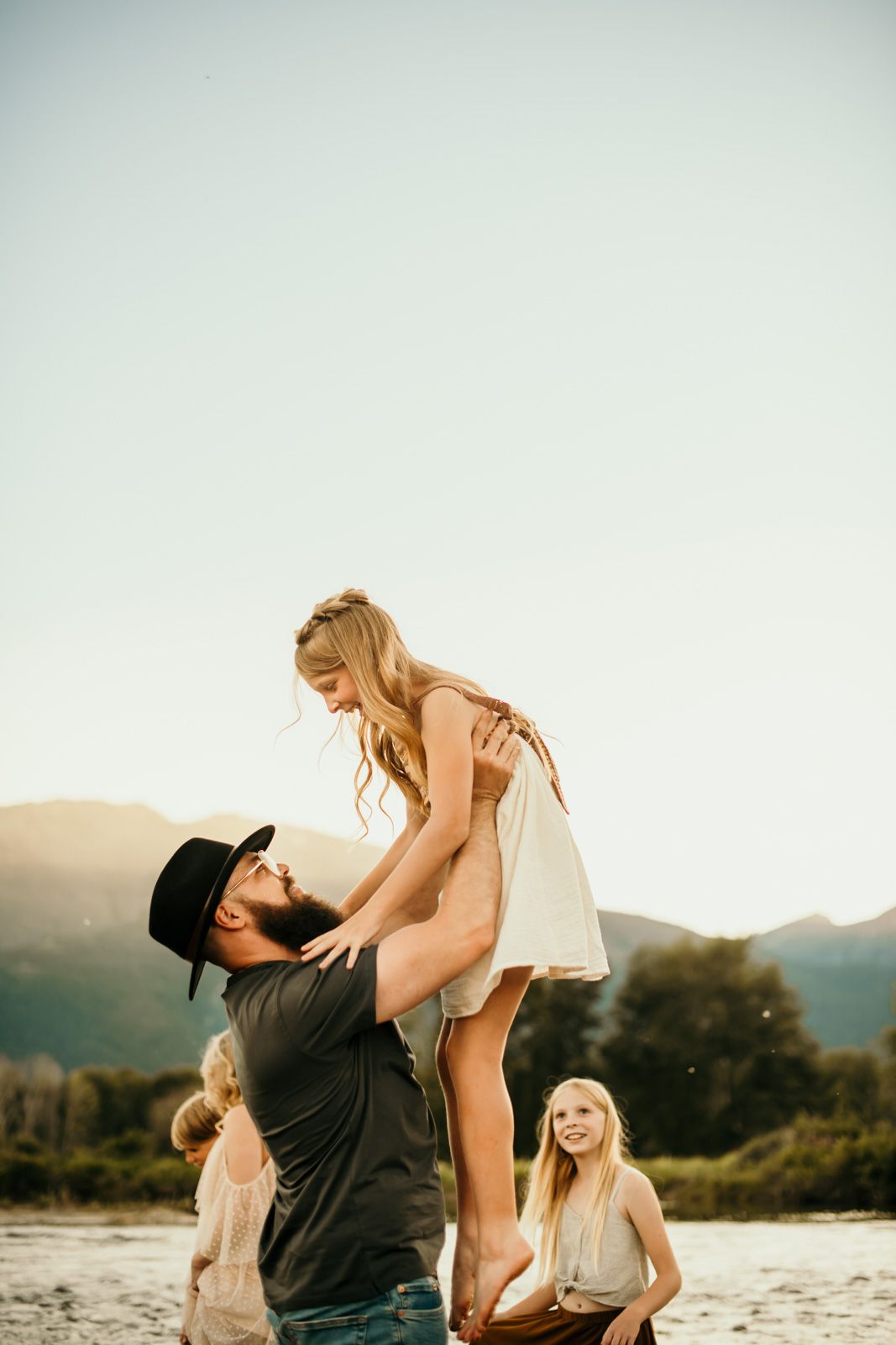 A couple shares playful moments together at sunset on a beach with mountains in the background.
