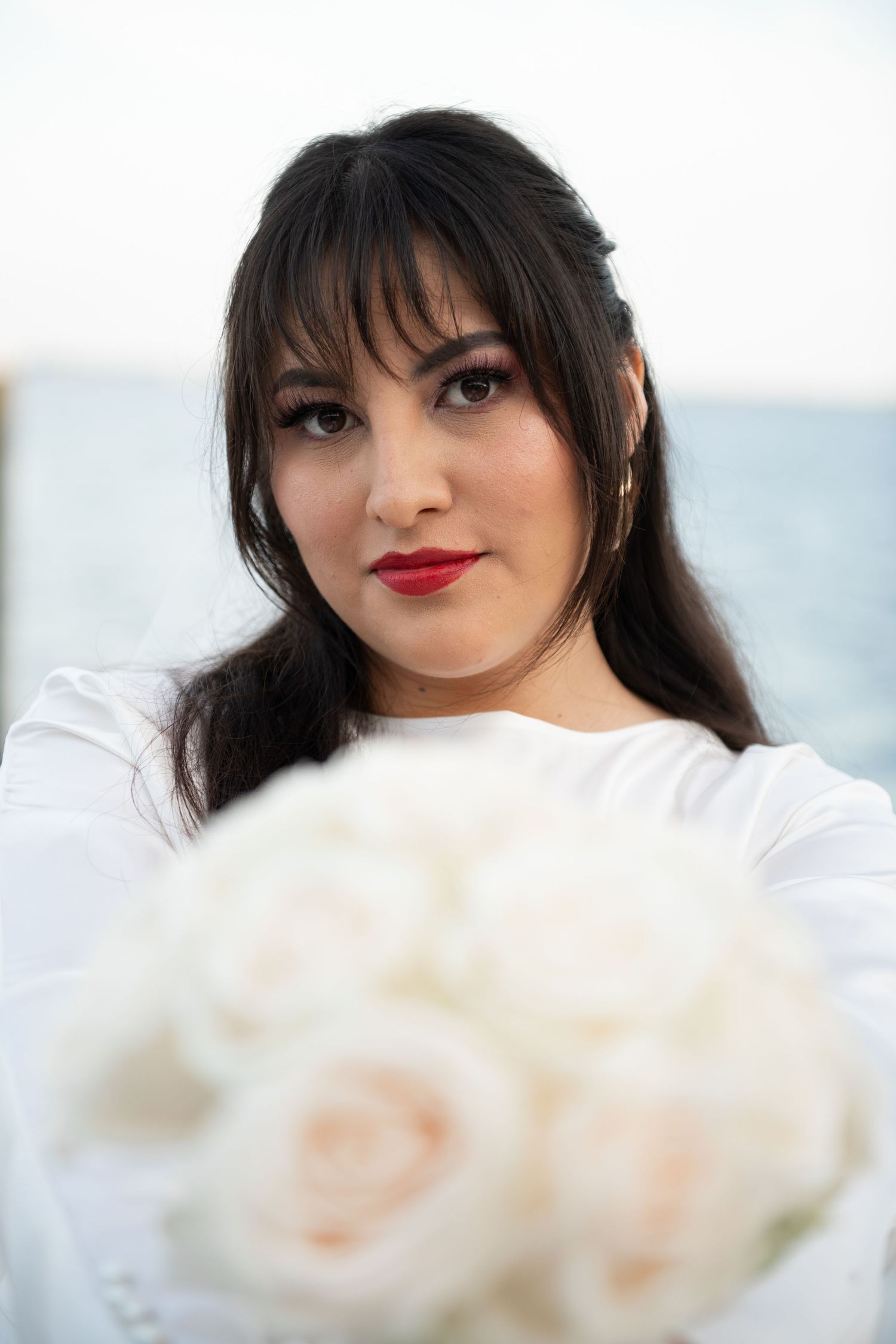 Close-up portrait with cream roses and red lipstick against white background.