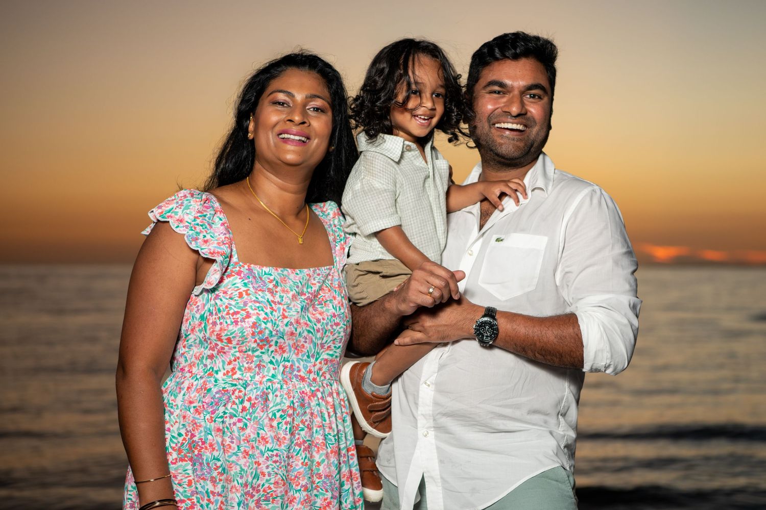 A family poses together on the beach during golden hour with the ocean as a backdrop. Beach photoshoot. Family photoshoot,