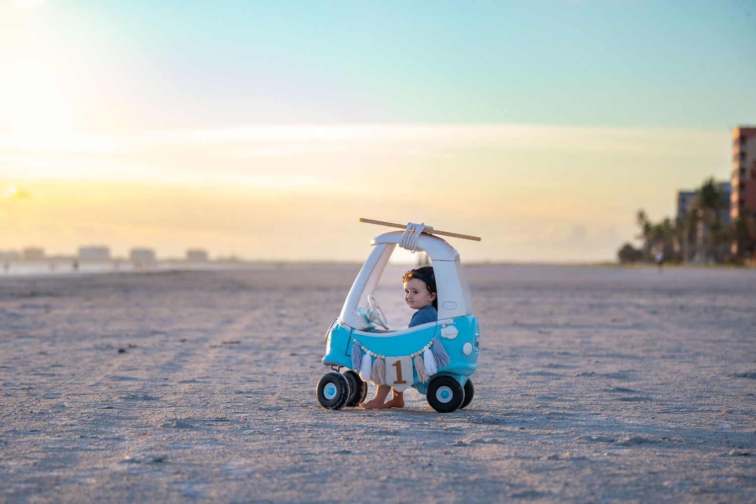 Toy vehicle photographed on beach with ocean and buildings in background.