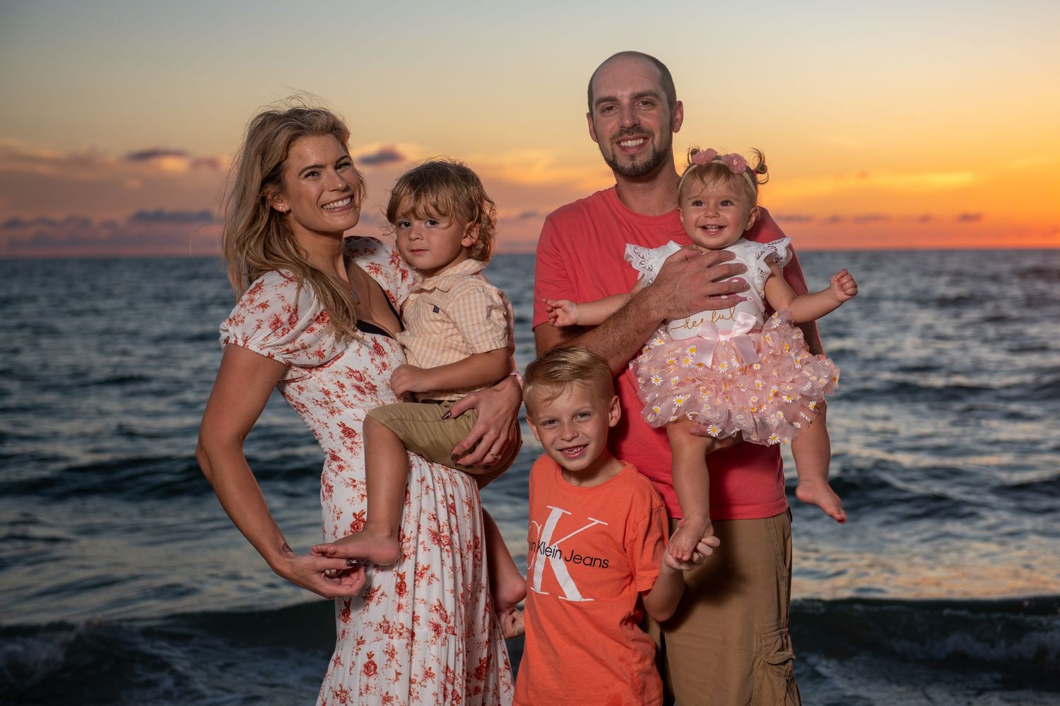 A family group poses together on the beach at sunset with the ocean as a backdrop.