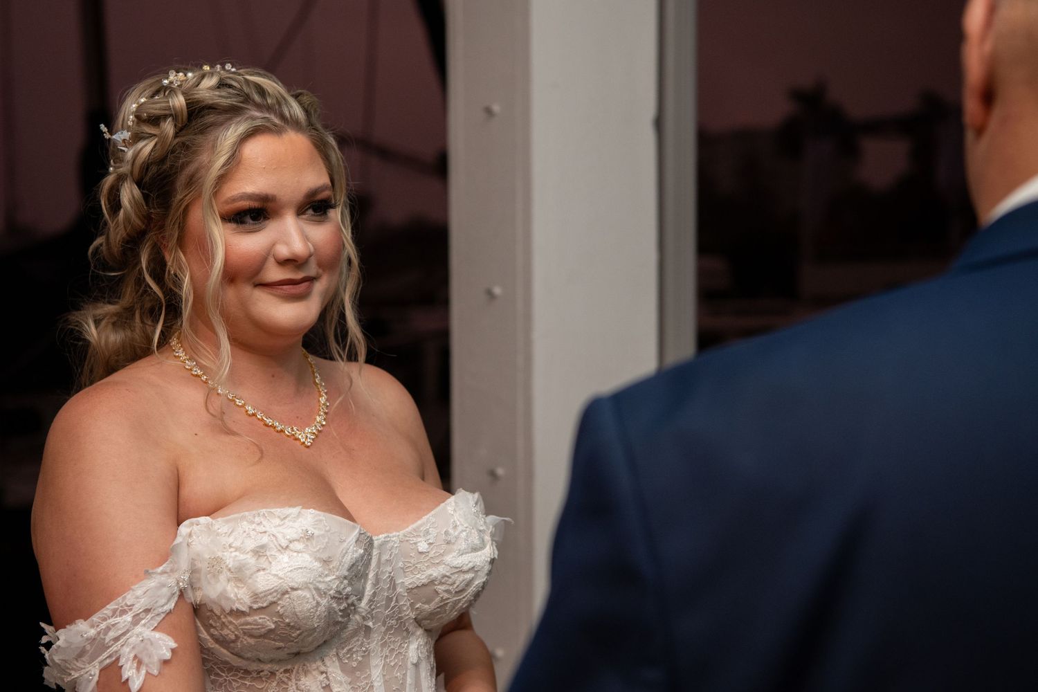 A bride in a beaded off-shoulder gown smiles during her wedding ceremony.