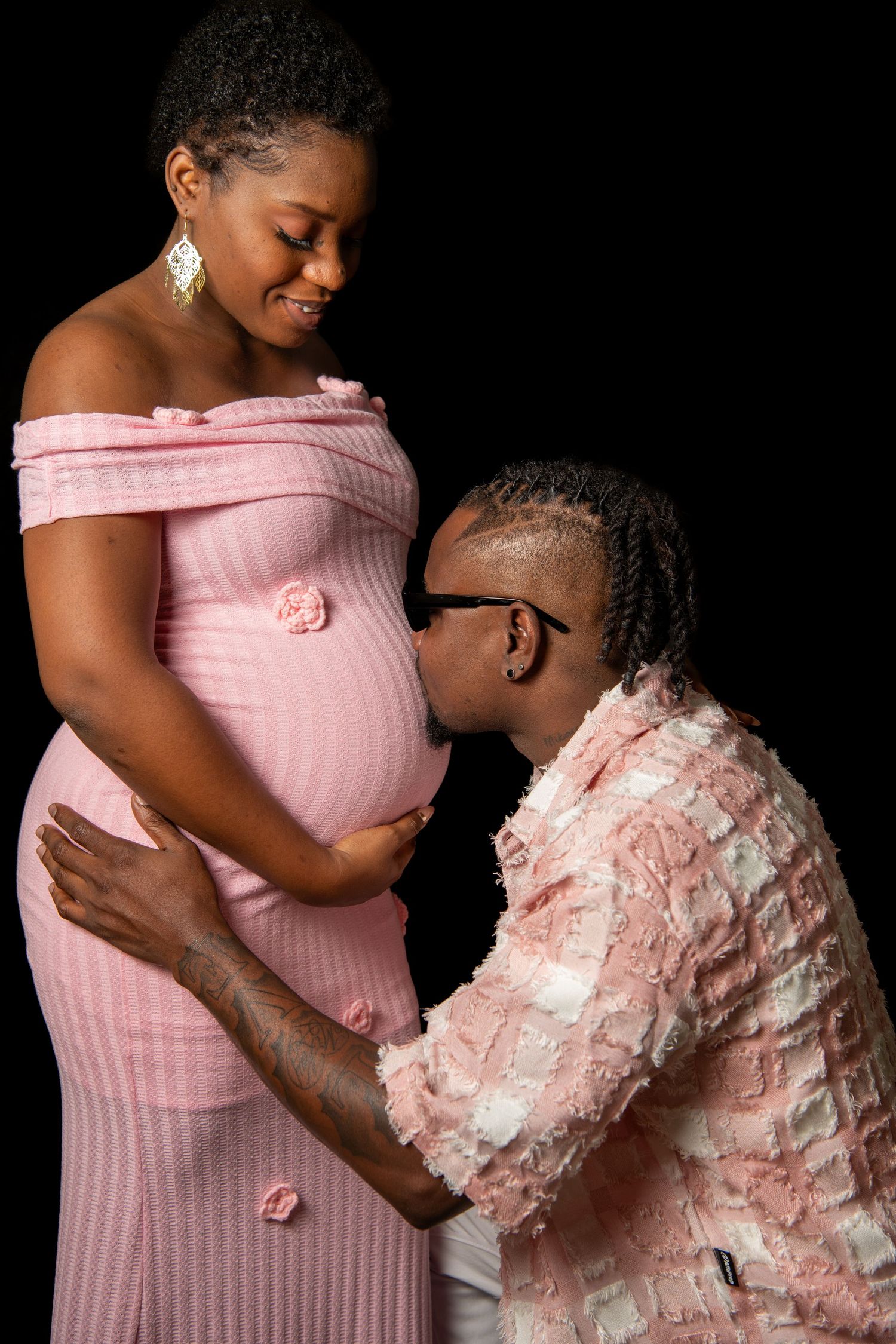 Maternity photo of couple in pink outfits against black background. Maternity photoshoot.