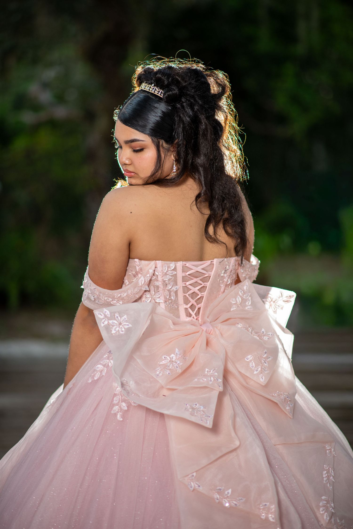 Back view of a pink ball gown with intricate lace details and corset-style ribbon closure. Quinceañera photos.