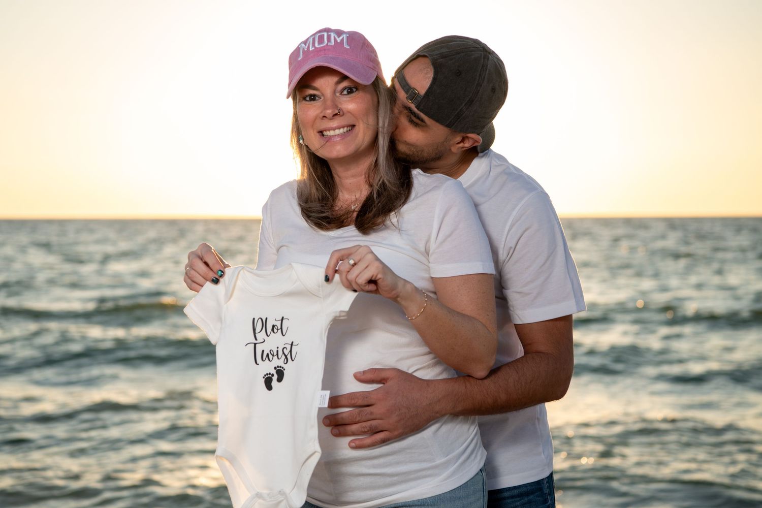 Pregnancy announcement photo with couple holding baby onesie on beach. Maternity photoshoot. Couples photos.