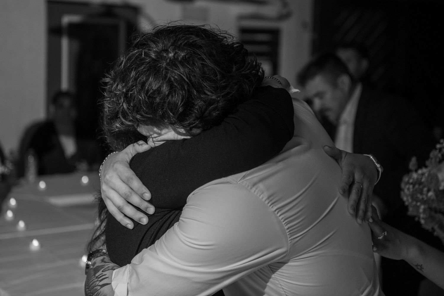 An emotional black and white photograph captures two people embracing at a wedding reception. Wedding photography.