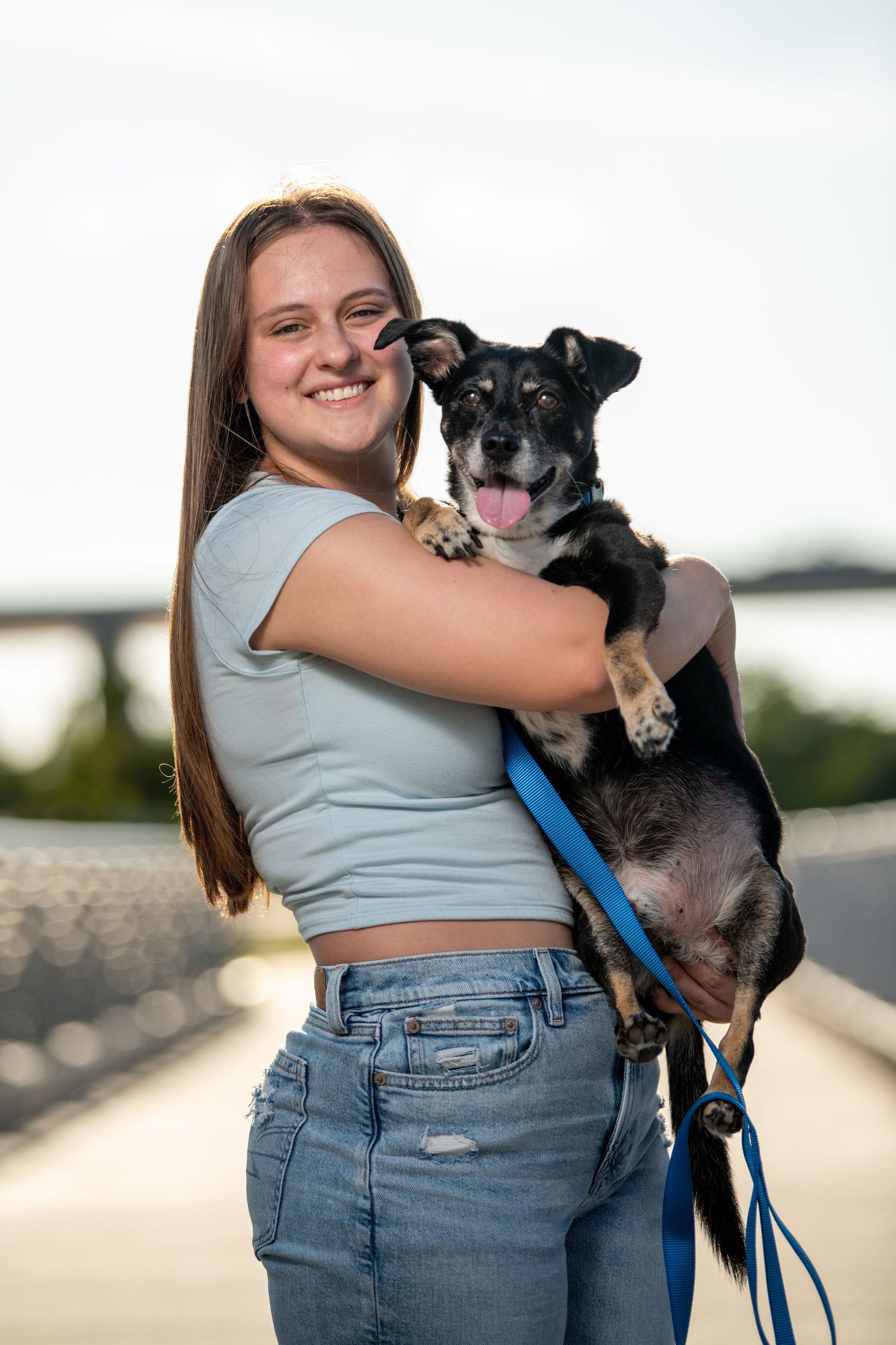 A person holds a happy black and white dog on a bridge walkway during sunset. Dog portraits. Self portraits.