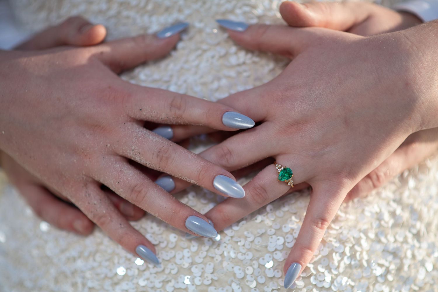 Close-up of hands showing engagement rings against sandy beach background. Engagement photoshoot. Couples photos.