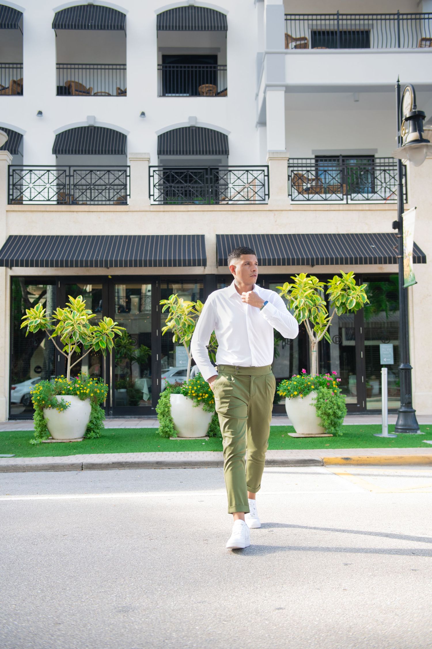 Professional man in business casual attire walking confidently outside a Mediterranean-style building with striped awnings.