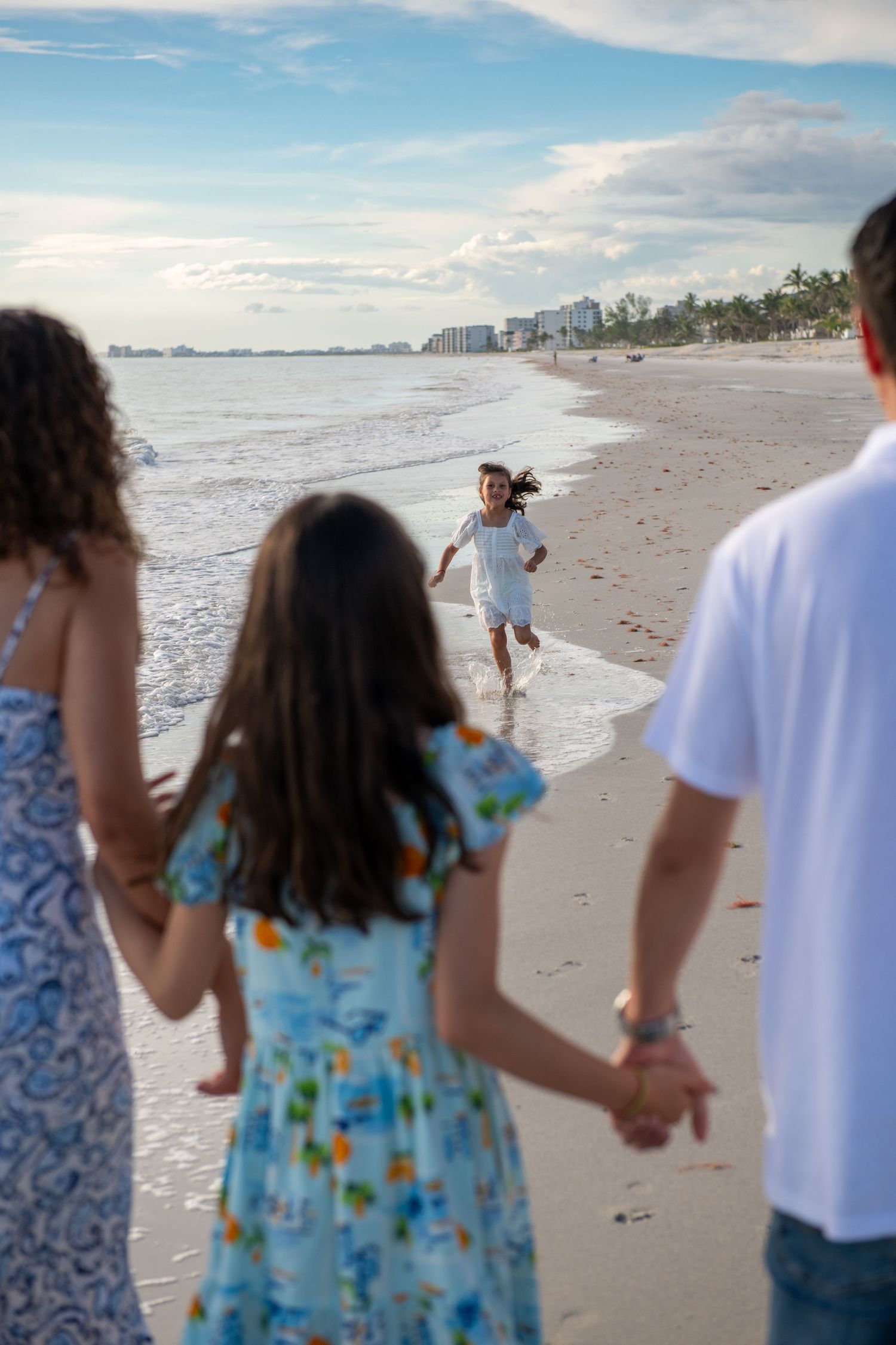 A child runs joyfully along the beach shoreline while others watch from behind.
