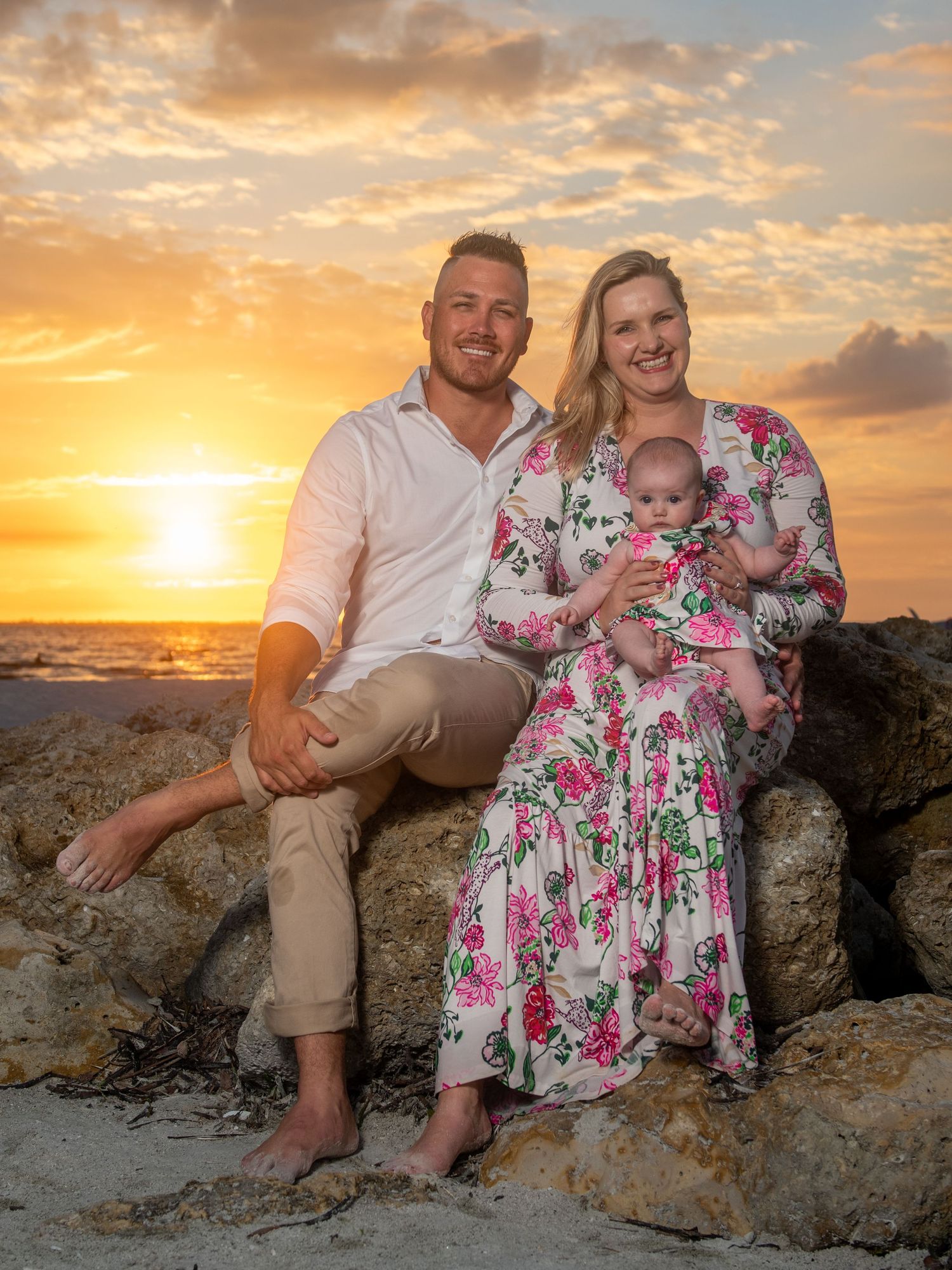 A family poses on rocky coastal formations during a vibrant sunset photoshoot.