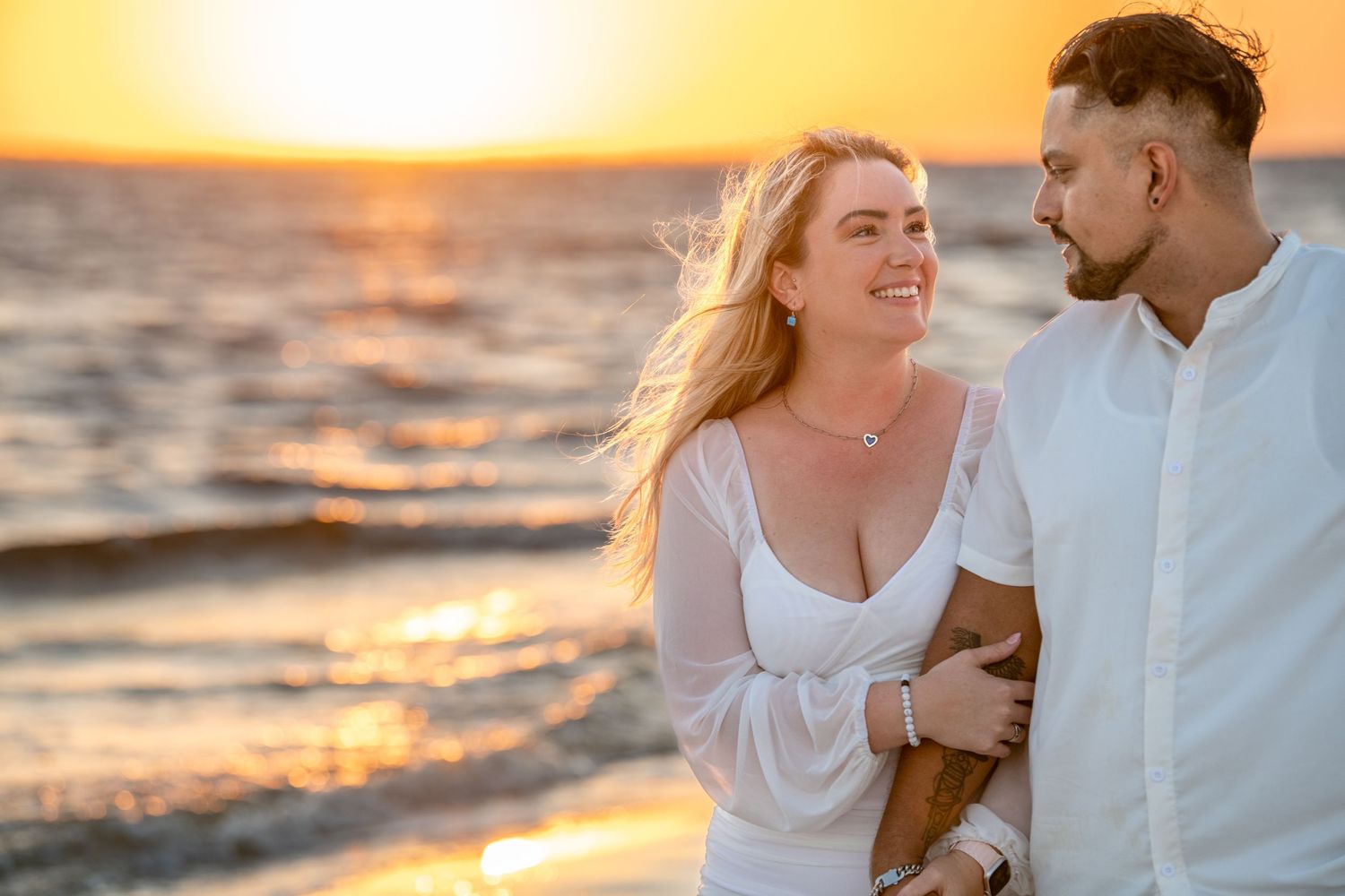 Joyful couple sharing laughter during sunset beach photoshoot with ocean views.
