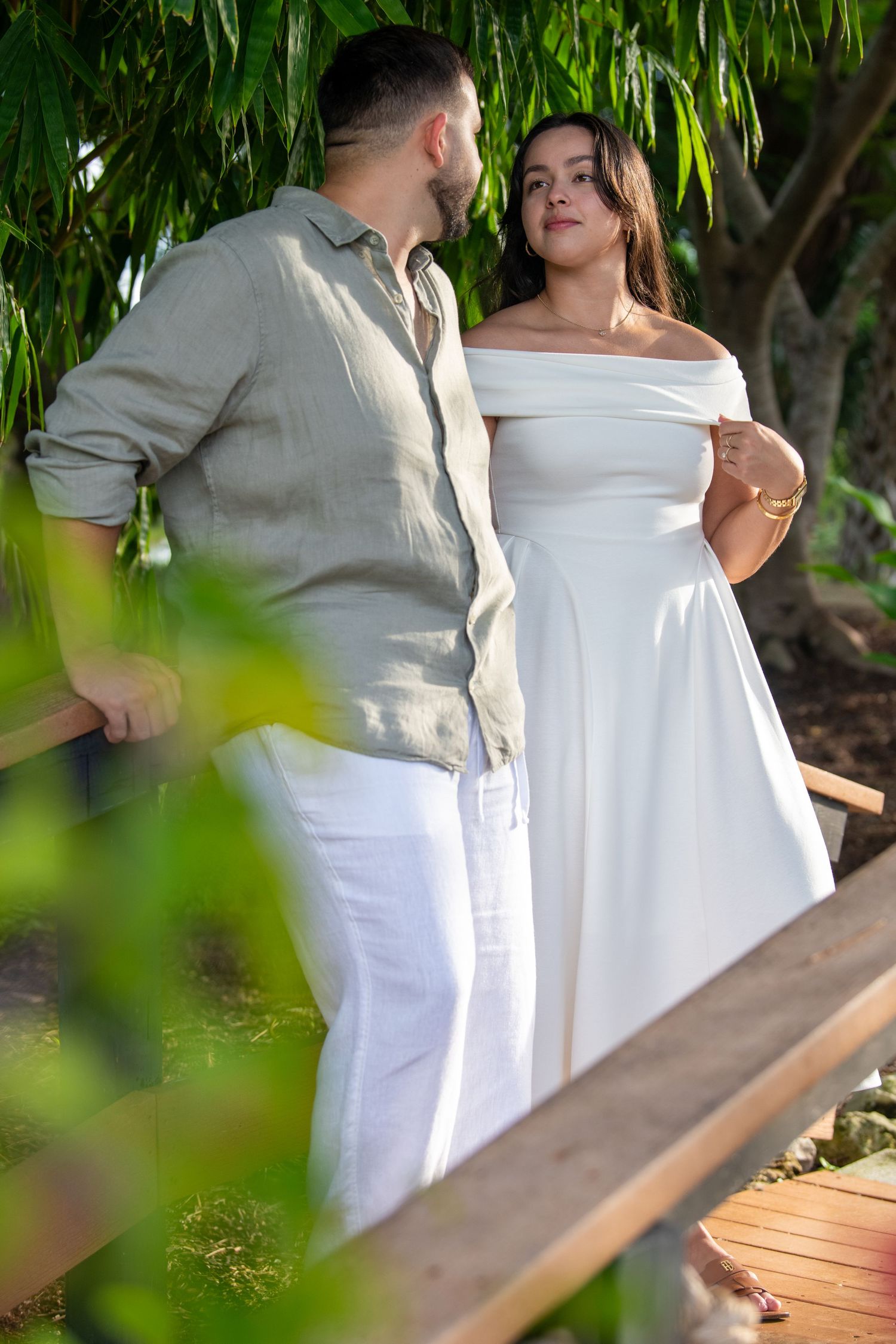 A couple in coordinated white and beige outfits share tender moments on a wooden deck.