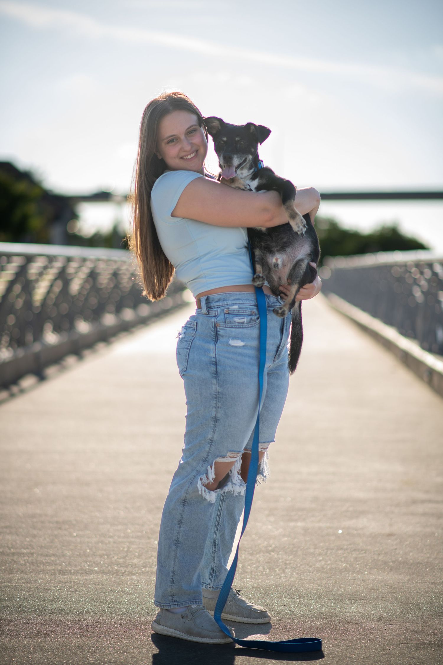 A person holds their black and white dog while standing on a bridge walkway. Dog portraits. Self portraits.