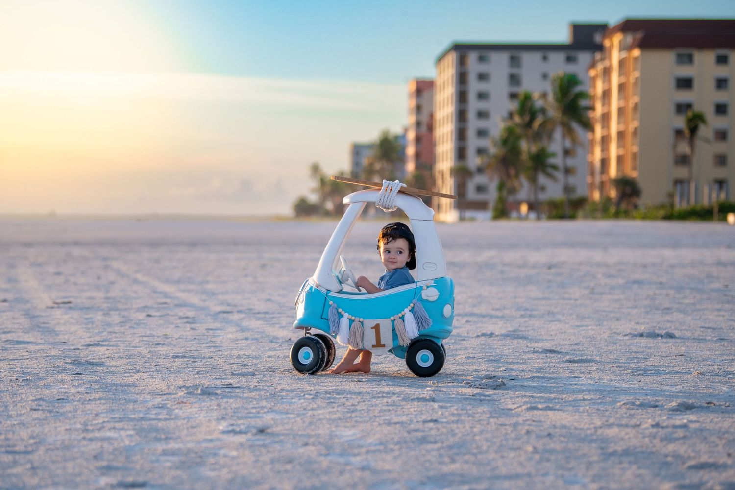 Miniature blue scooter prop on sandy beach with condominiums in background.