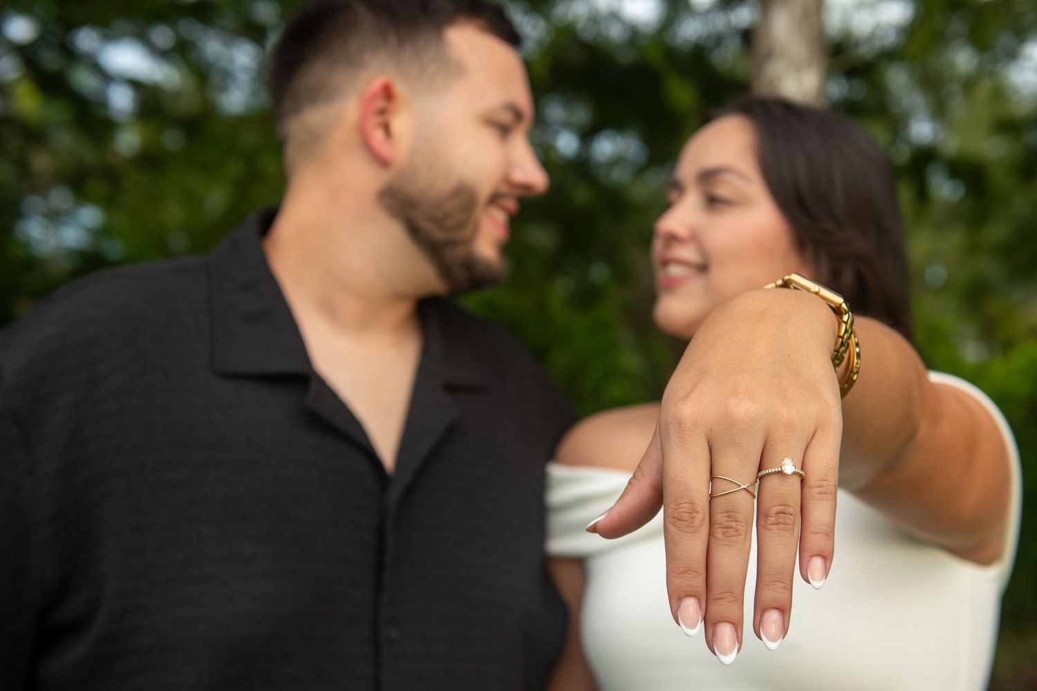 A couple shares intimate moments in a garden setting while showing off an engagement ring.