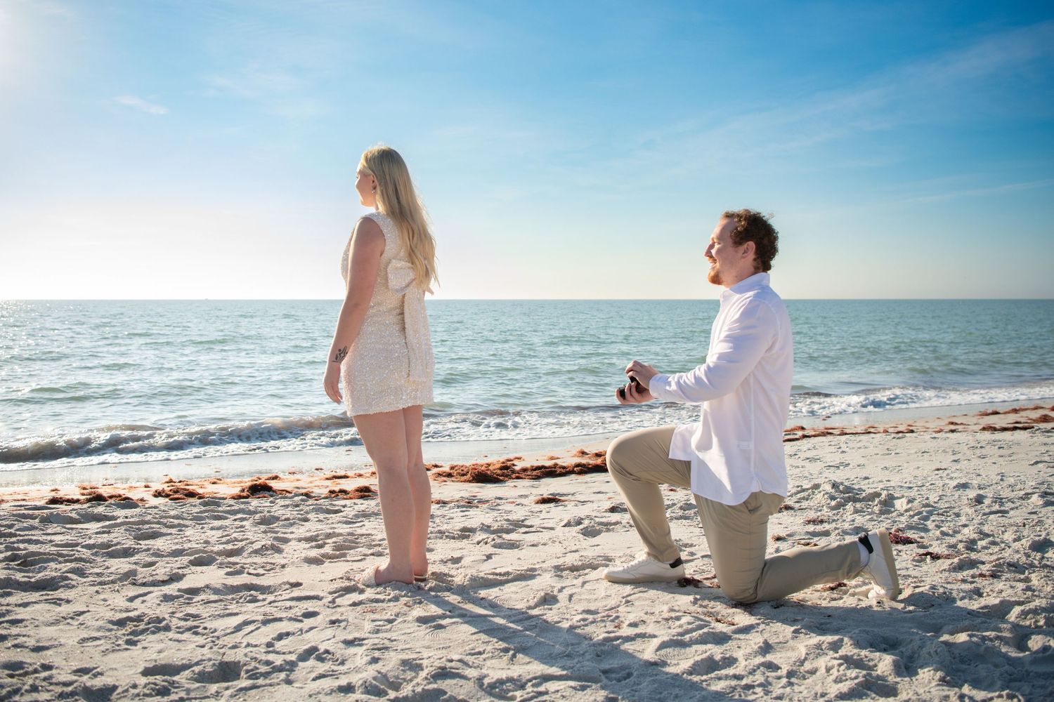 A surprise proposal moment captured on a sunny beach with the ocean in the background. Engagement photoshoot. Couples photos.