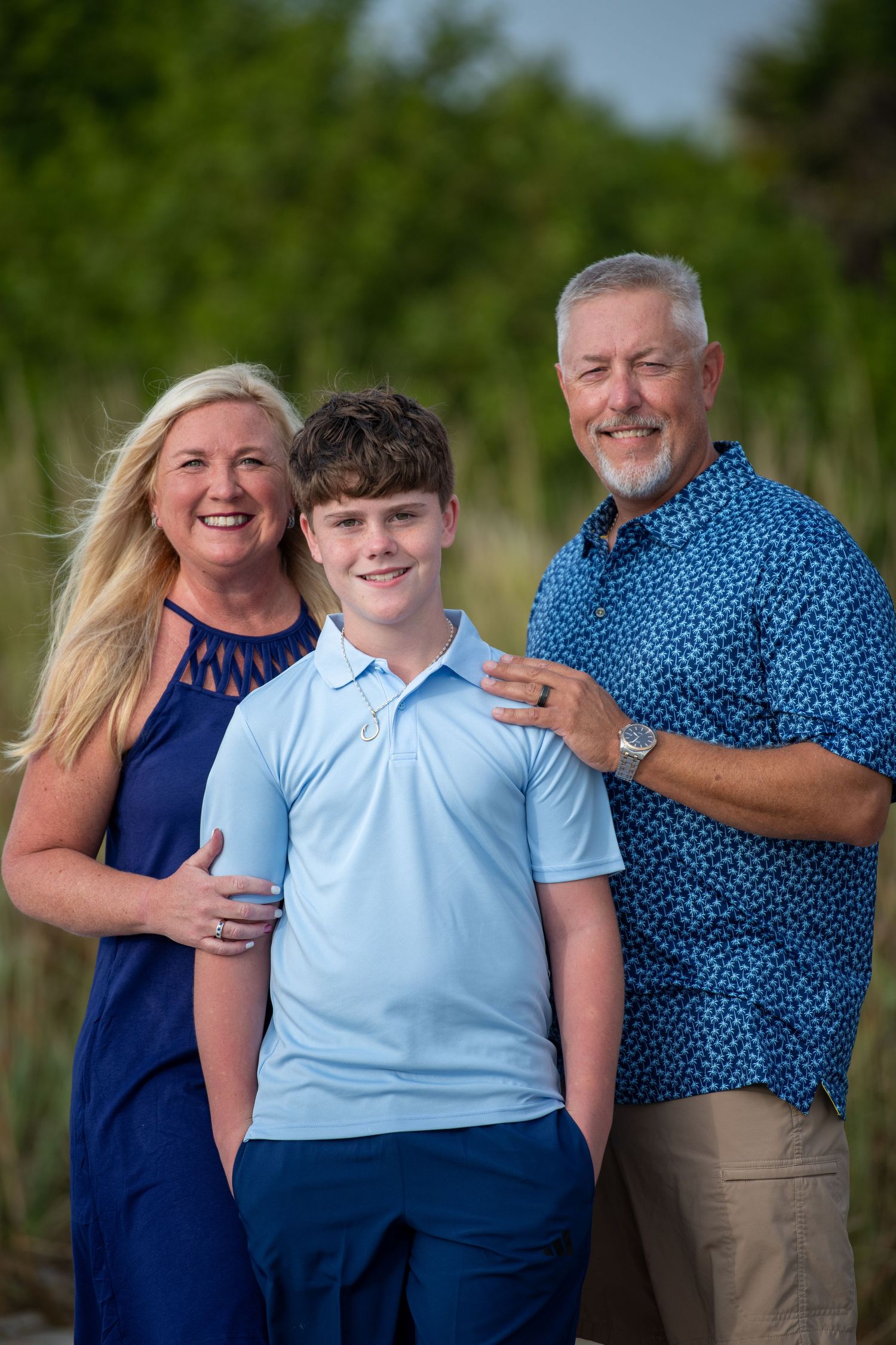 A family of three poses together outdoors against a natural green background. Family photoshoot.