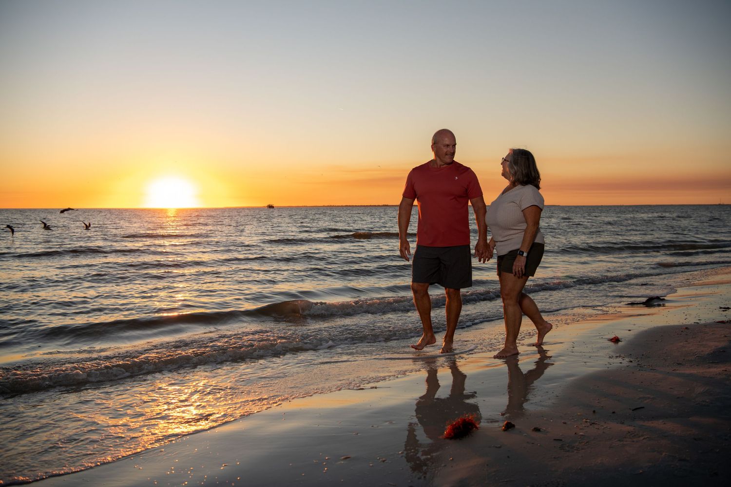 Silhouettes walking along beach shore during vibrant orange sunset. Couples photoshoot.