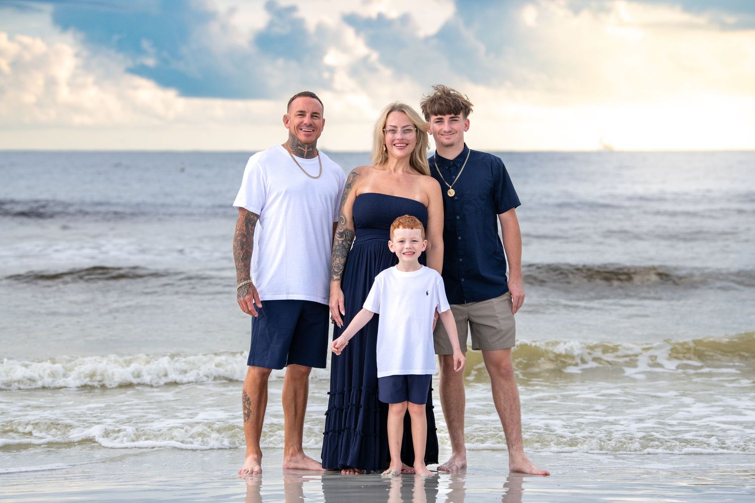 Family enjoying a sunset photoshoot on a white sandy beach with ocean waves in the background.