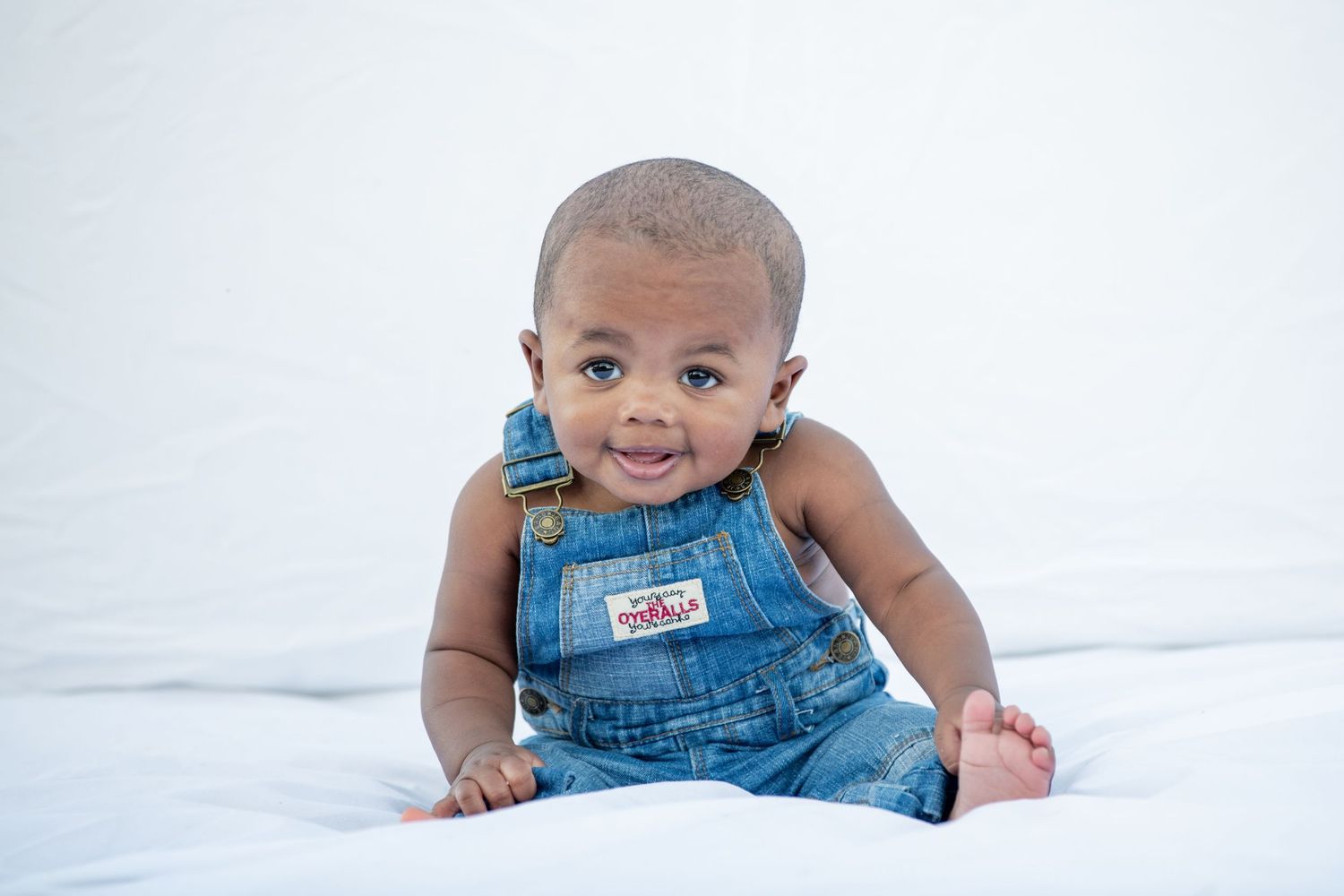 Infant wearing denim overalls crawls on white background.