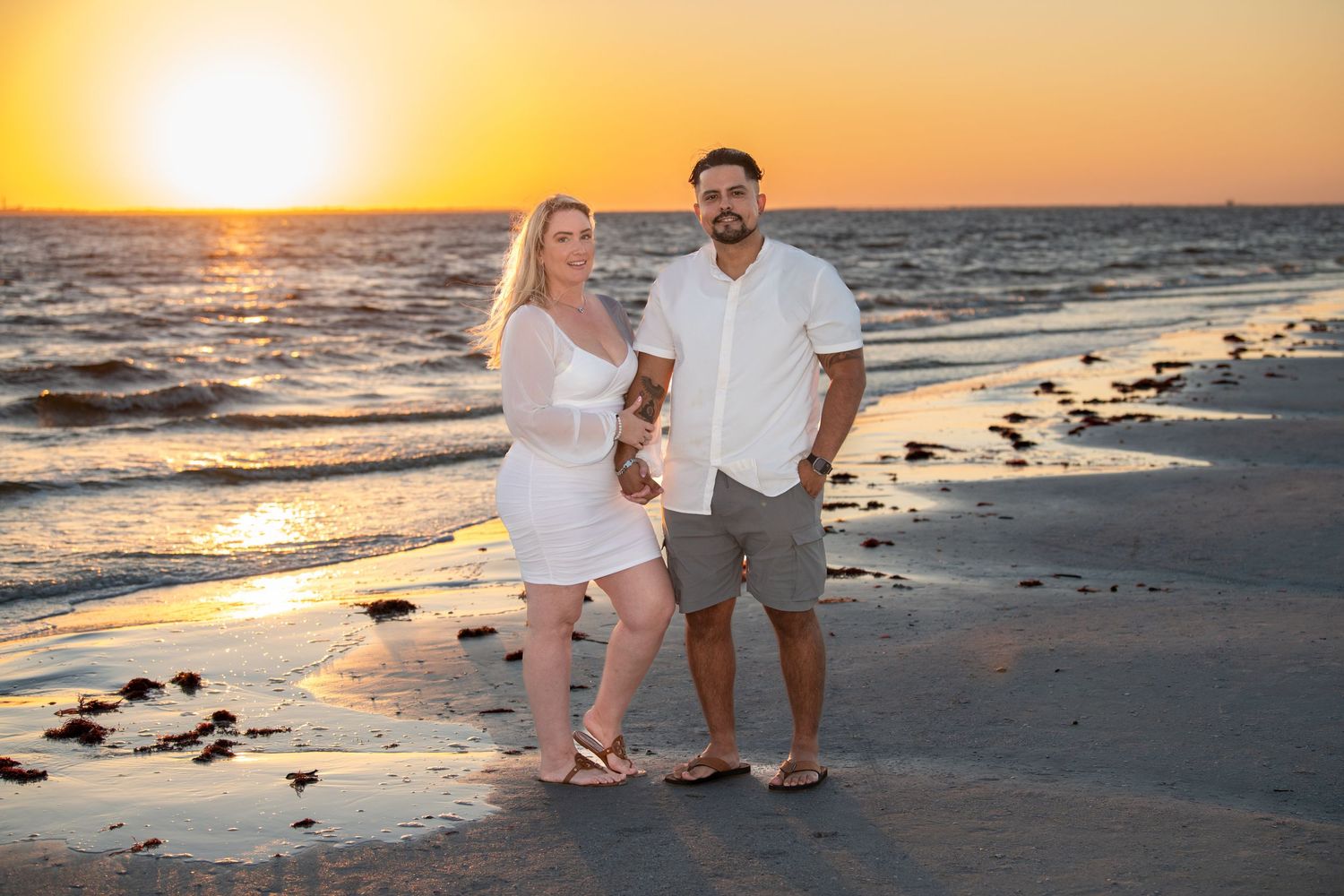 Couple enjoying a sunset moment together on a sandy beach with waves in the background.