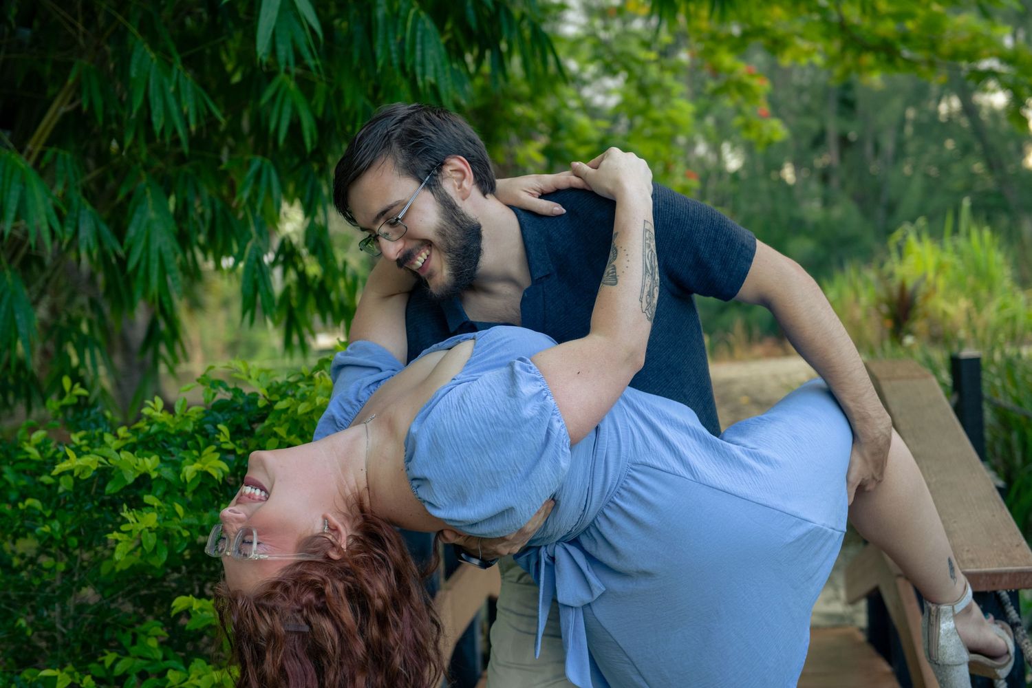 Couple sharing an intimate moment on a wooden bench surrounded by lush greenery.
